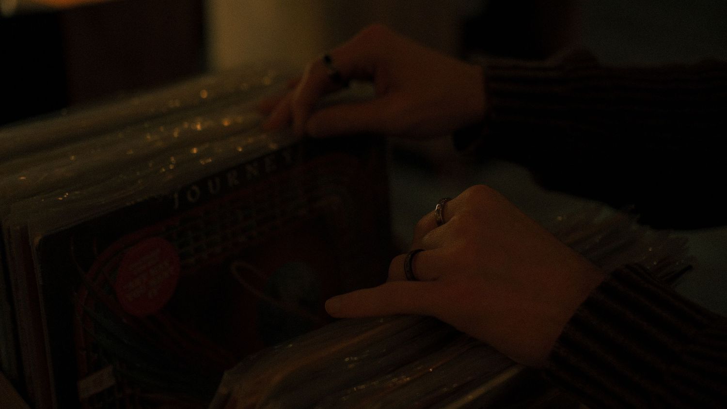 Close-up of hands carefully browsing through vinyl records in a dimly lit record store.