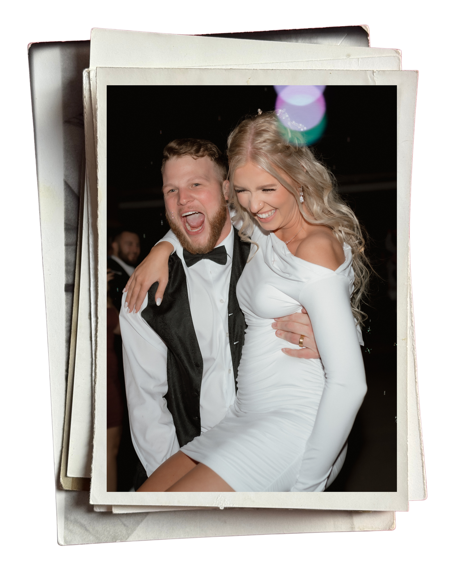 Joyful couple in formal attire laughing at wedding reception, man in tuxedo carrying woman in white dress.