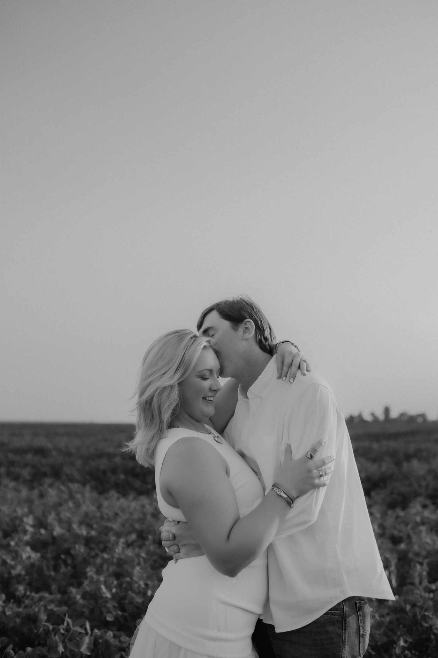 Black and white portrait of couple embracing romantically in an open field at dusk.
