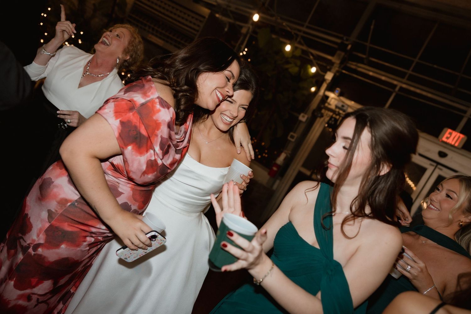Bride dancing joyfully with guests in floral and green dresses at wedding reception.