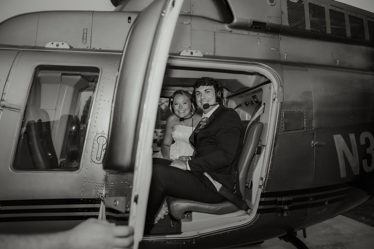 Bride and groom share a joyful moment seated inside a vintage helicopter in black and white photo.