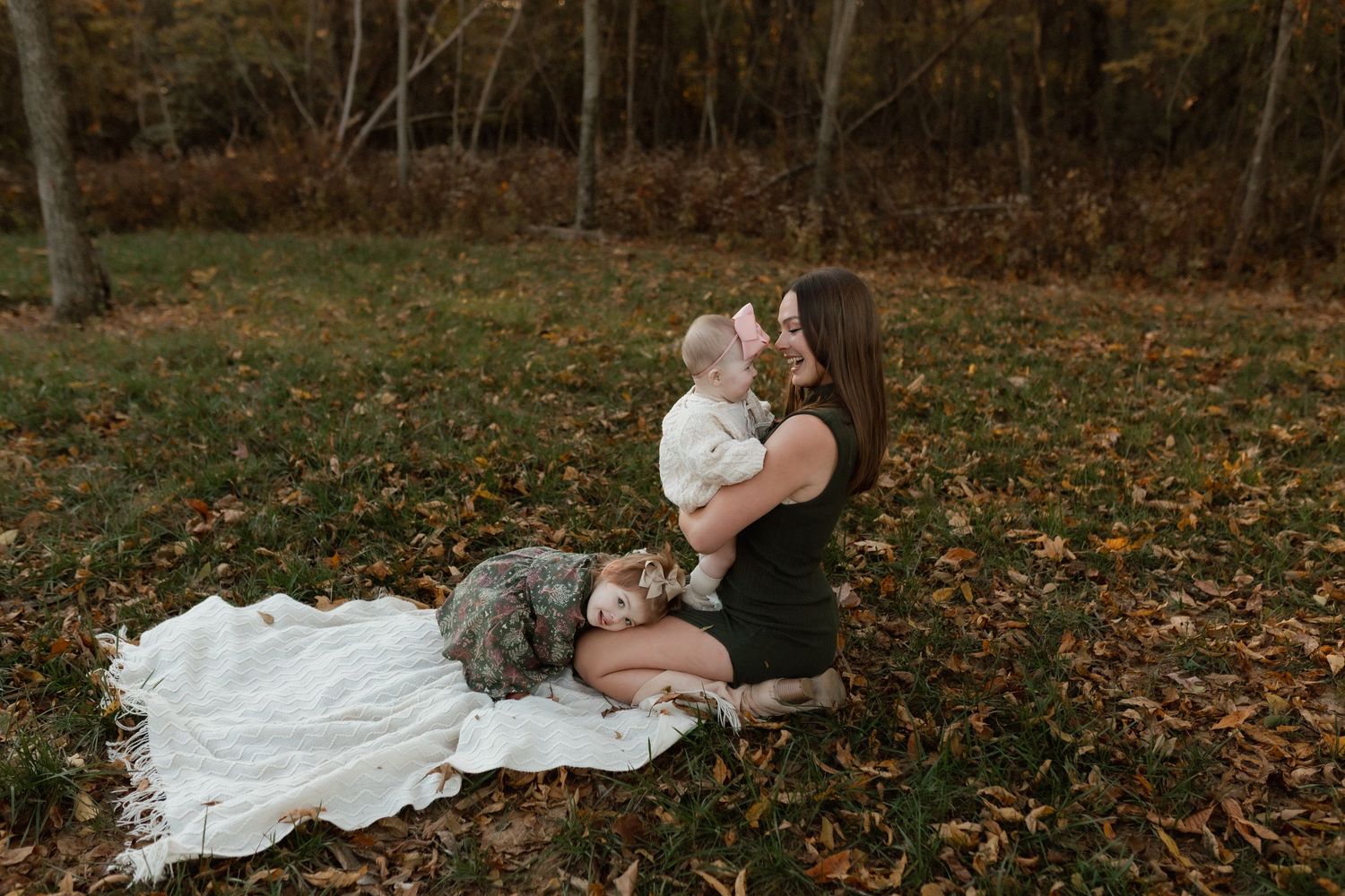 Mother sitting on a blanket in autumn park, lovingly holding her baby among fallen leaves.