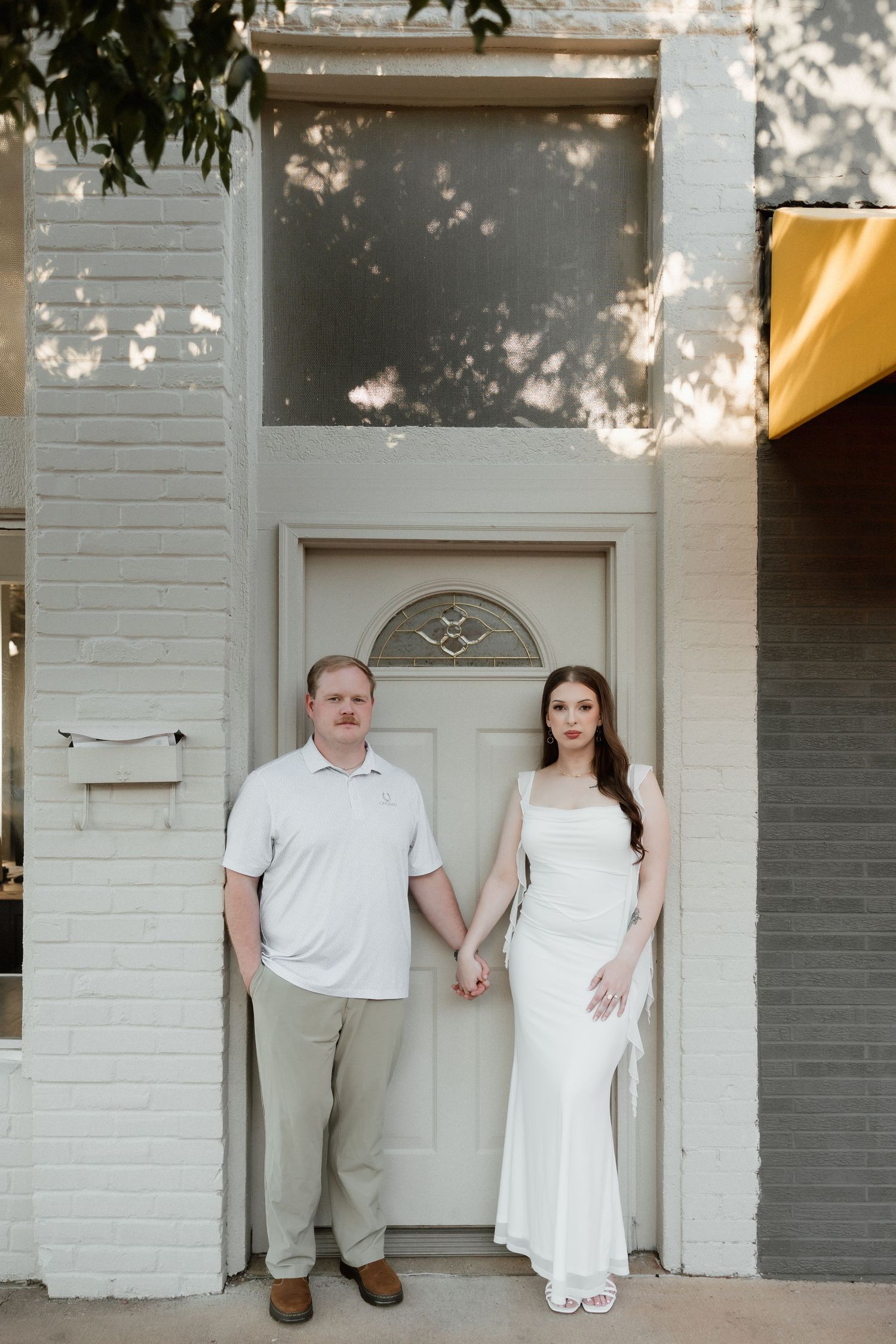 A couple holds hands while standing in front of a charming white brick building entrance.