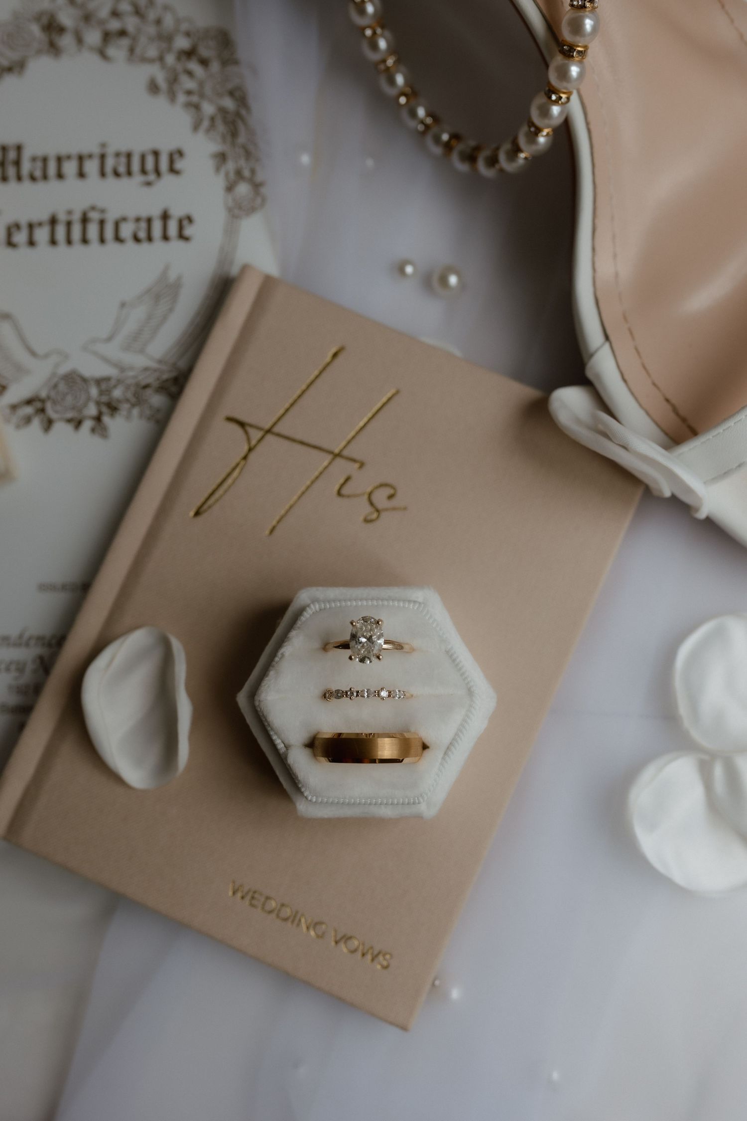 Wedding rings in a velvet box on a His vows book beside a marriage certificate.