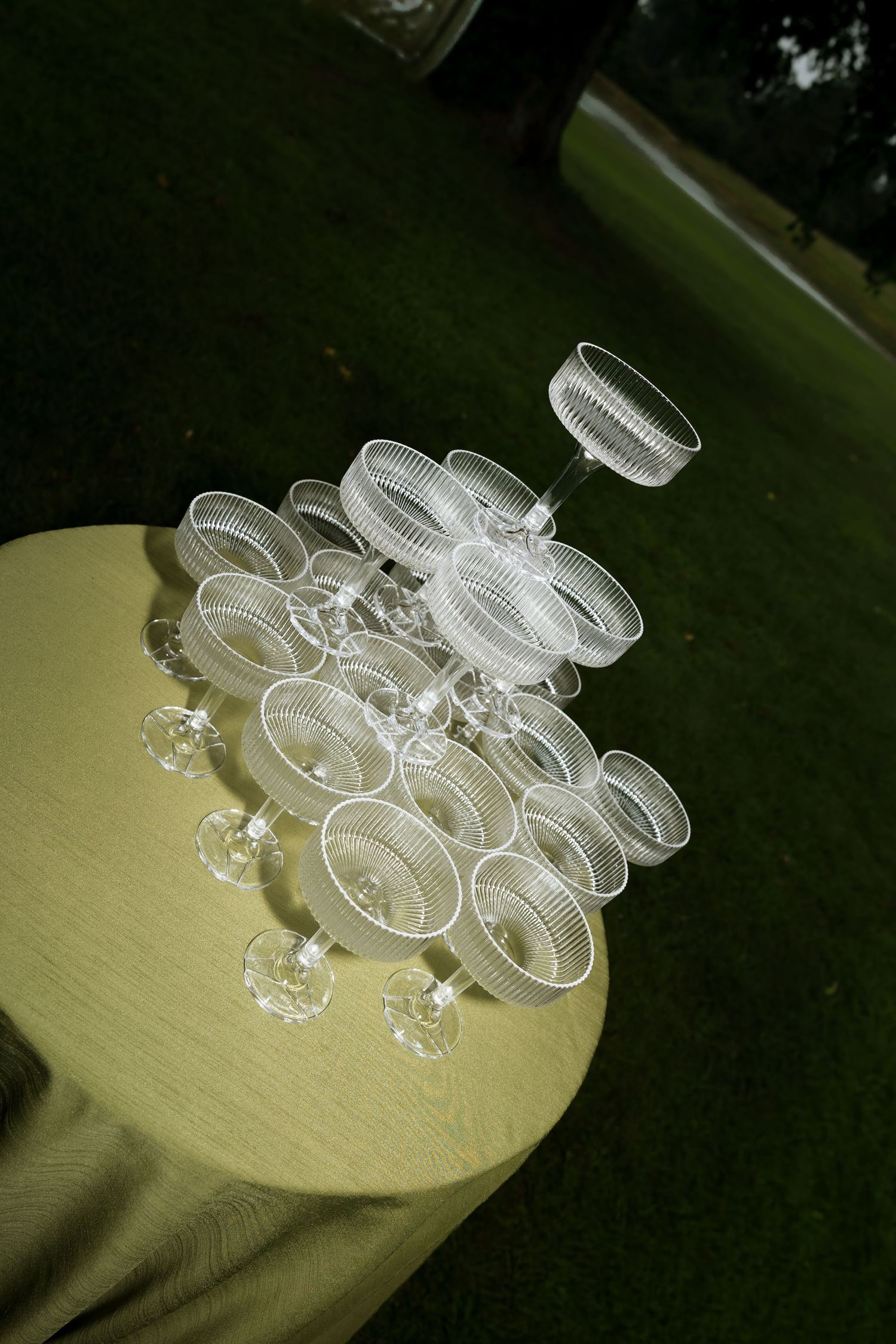 Elegant tower of crystal champagne coupe glasses stacked on a table at an outdoor event.