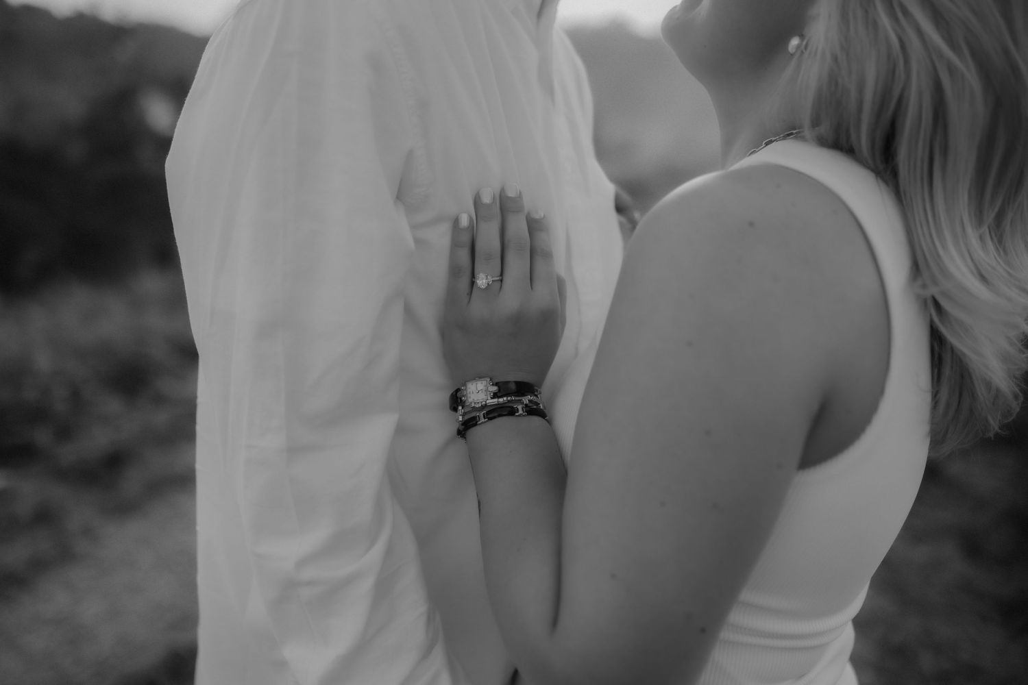 Black and white close-up of bride resting hand on grooms white shirt showing bracelet.