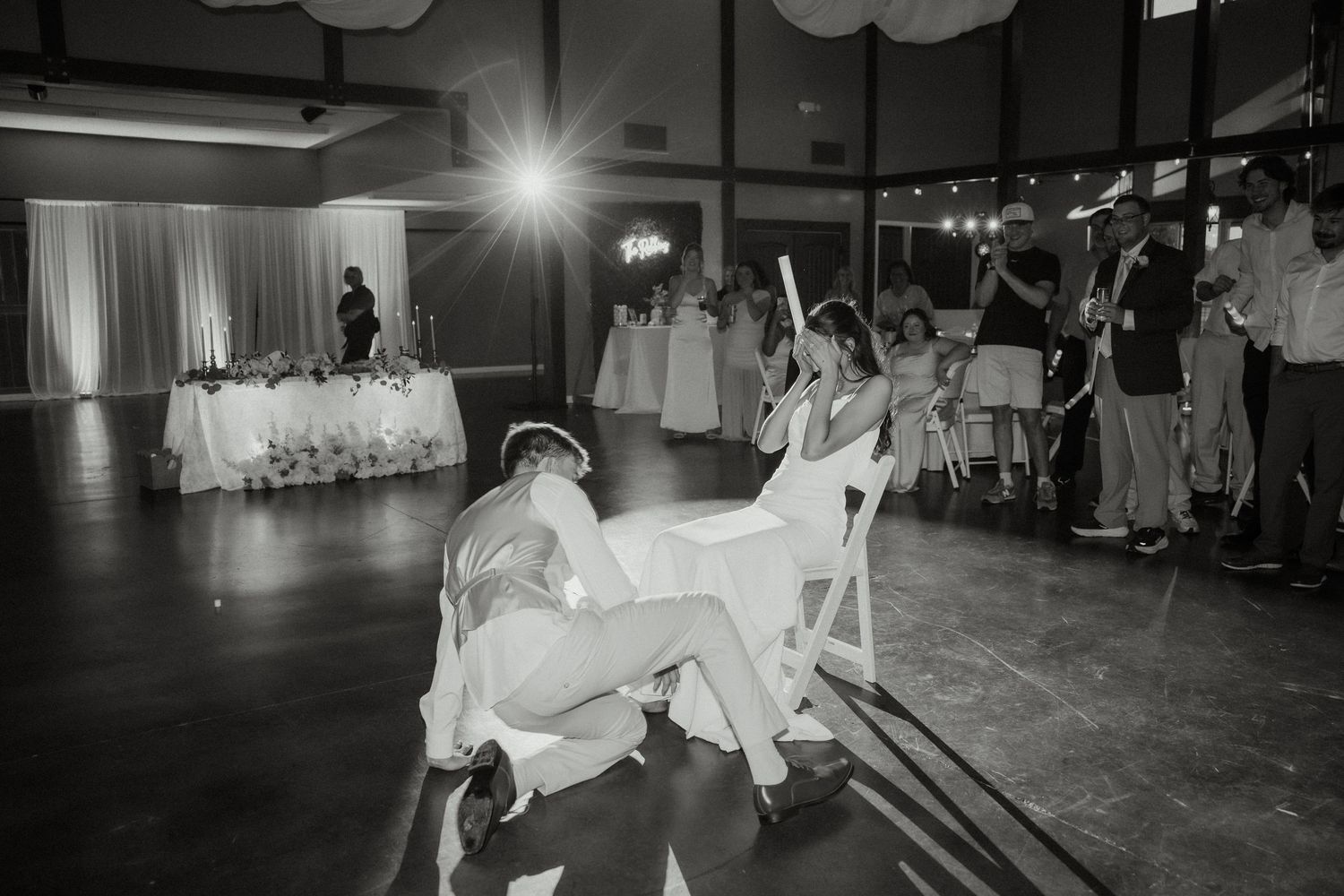 Bridesmaids competing in fun chair game on wedding reception dance floor in black and white.