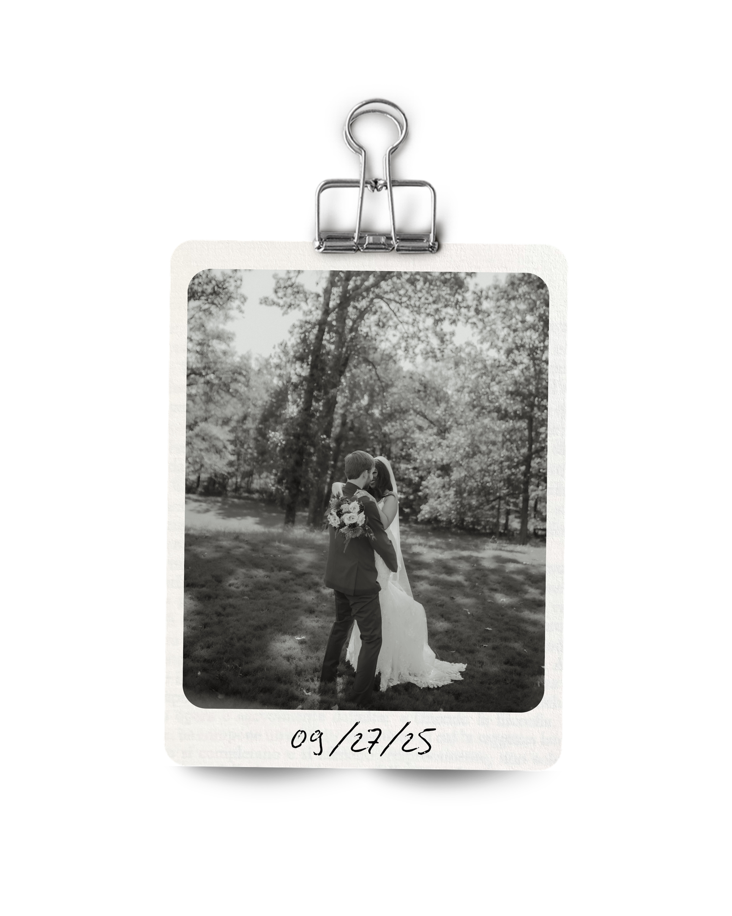 Black and white polaroid photo of bride and groom embracing in a lush outdoor setting dated 09/27/25.