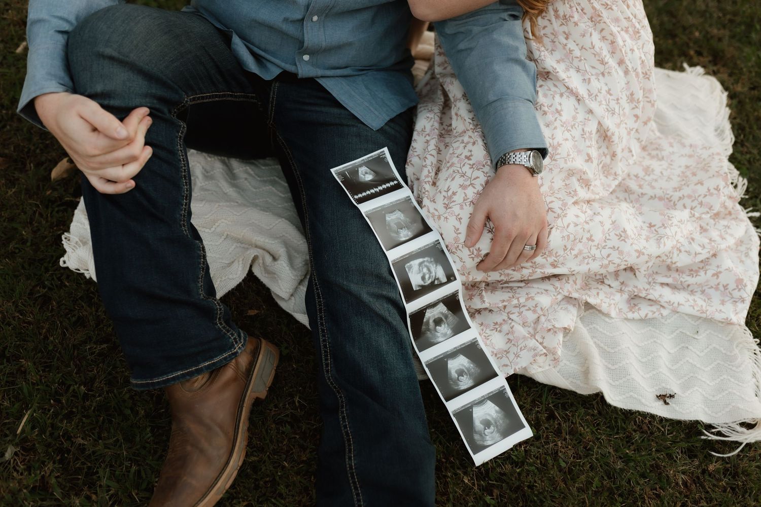 Close-up of couple holding ultrasound strip photos while sitting on grass outdoors.