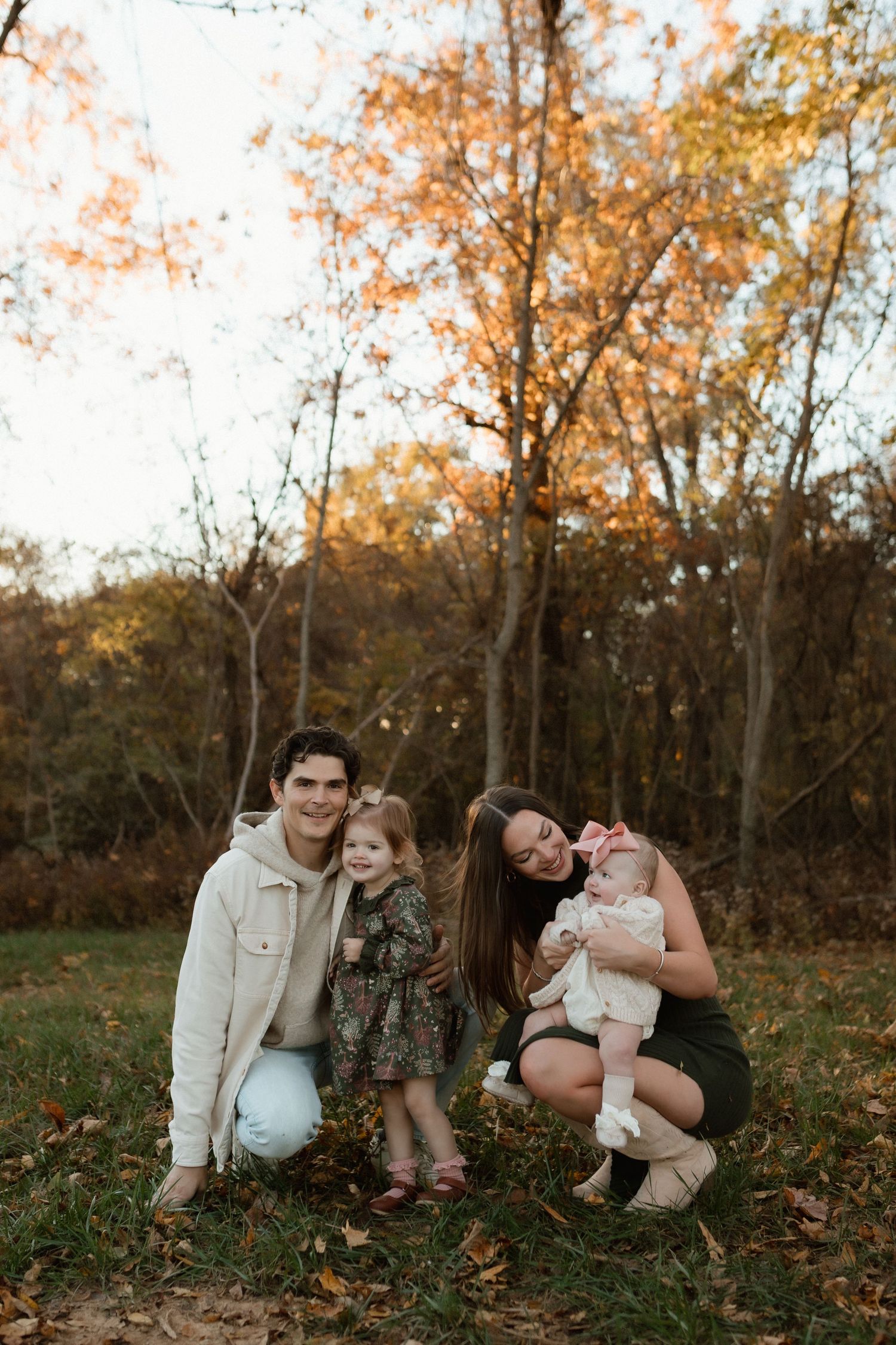 Happy family of four posing together in an autumn park with colorful fall foliage in the background.
