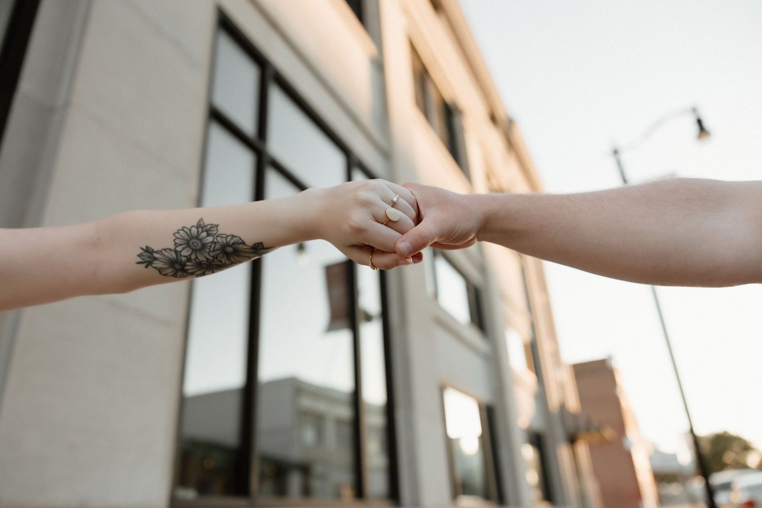 Two people reach out to hold hands on an urban street, one hand featuring a floral tattoo.