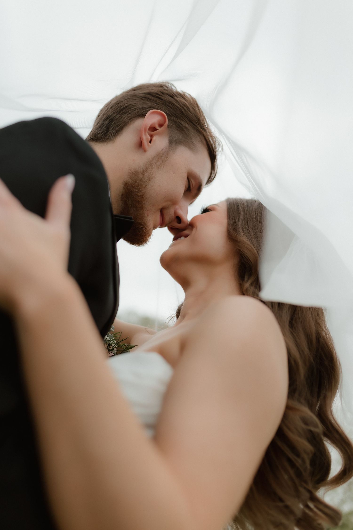 Bride and groom share a romantic kiss under the bride's flowing veil on wedding day.