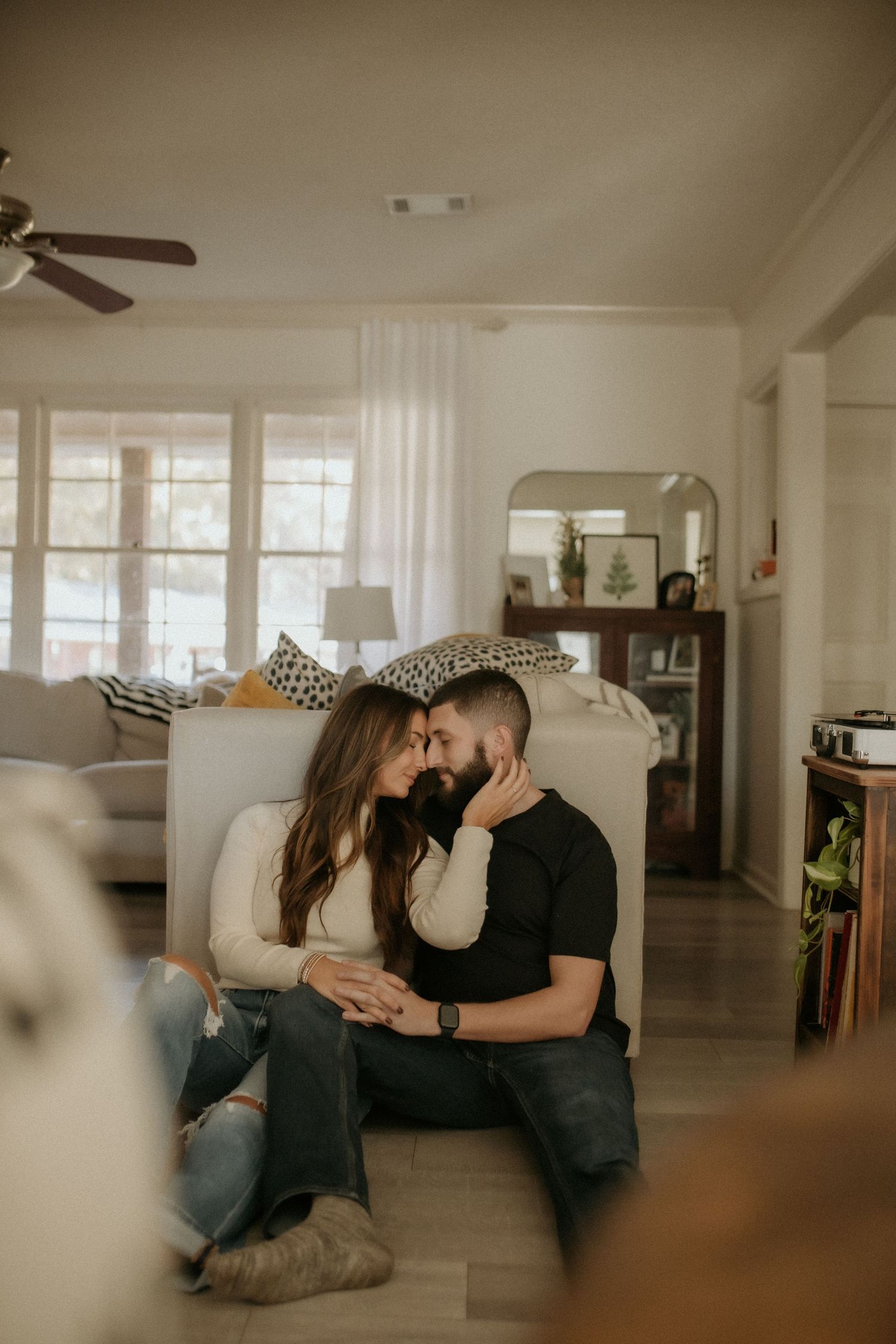 Couple leans in for a kiss while sitting on the floor of a bright, cozy living room.