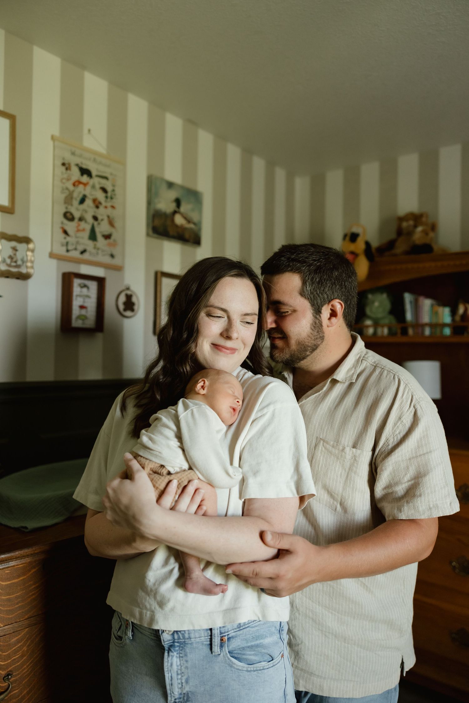 New parents tenderly holding their sleeping newborn in a warmly decorated striped nursery.