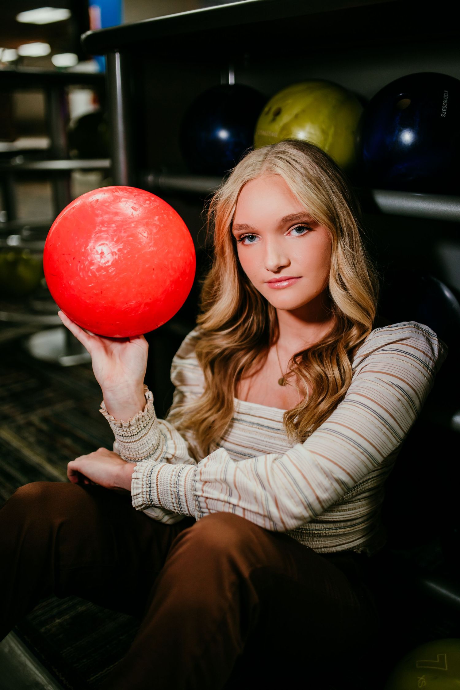 Young blonde woman holding a red bowling ball at a bowling alley.