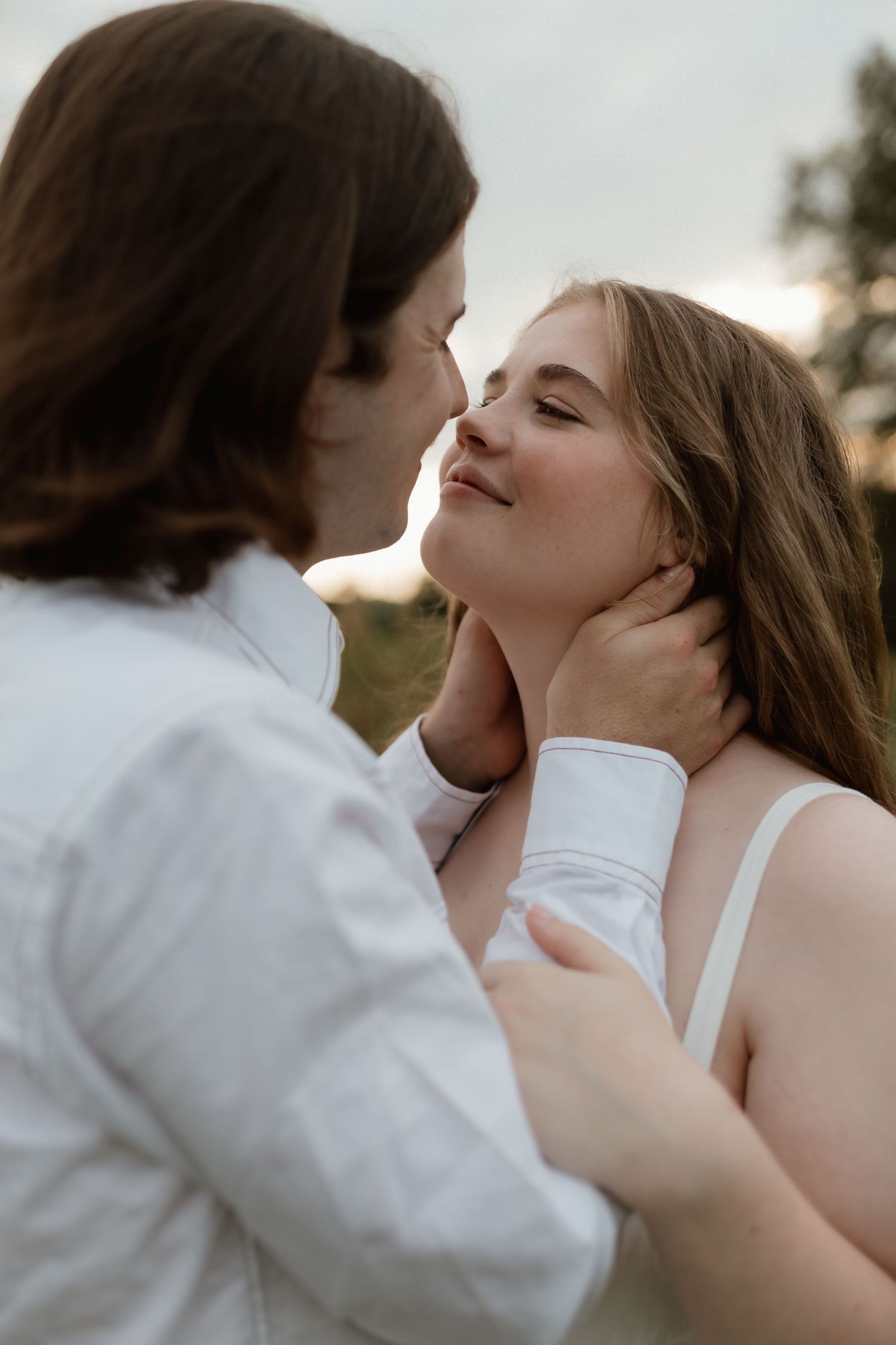 Intimate close-up of couple about to kiss outdoors at dusk, man gently holding womans face in his hands.