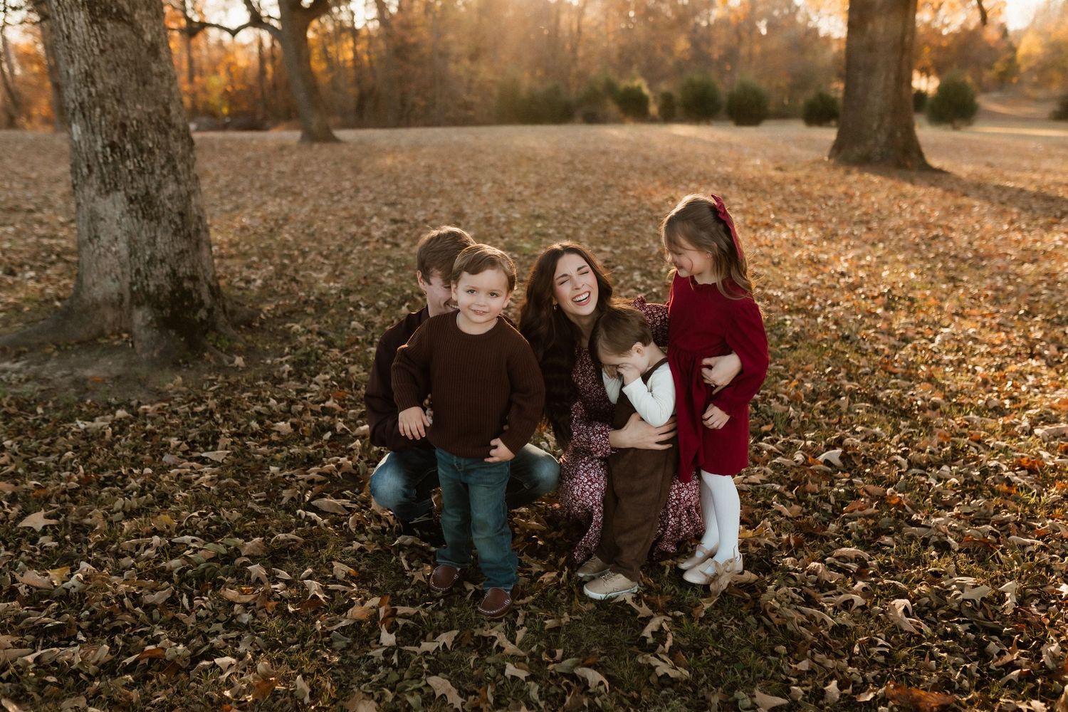 Mother sits on autumn leaves surrounded by her three children during a warm golden hour family portrait session.
