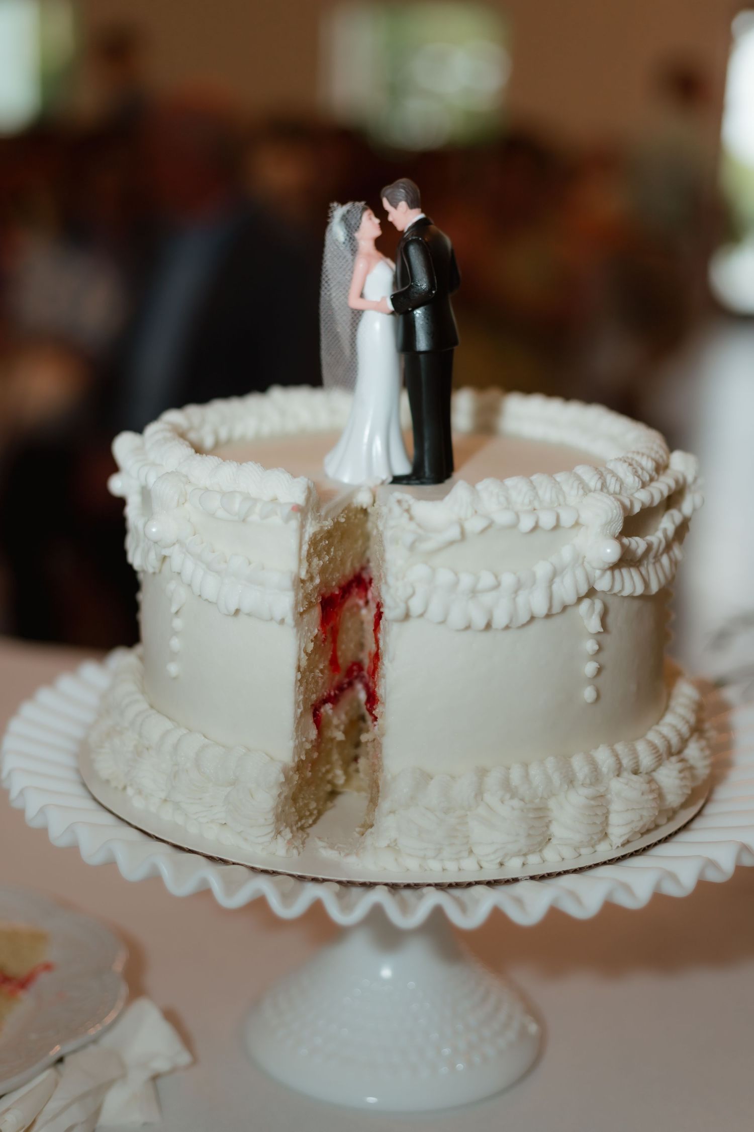 Classic white wedding cake with bride and groom topper on a milk glass cake stand.