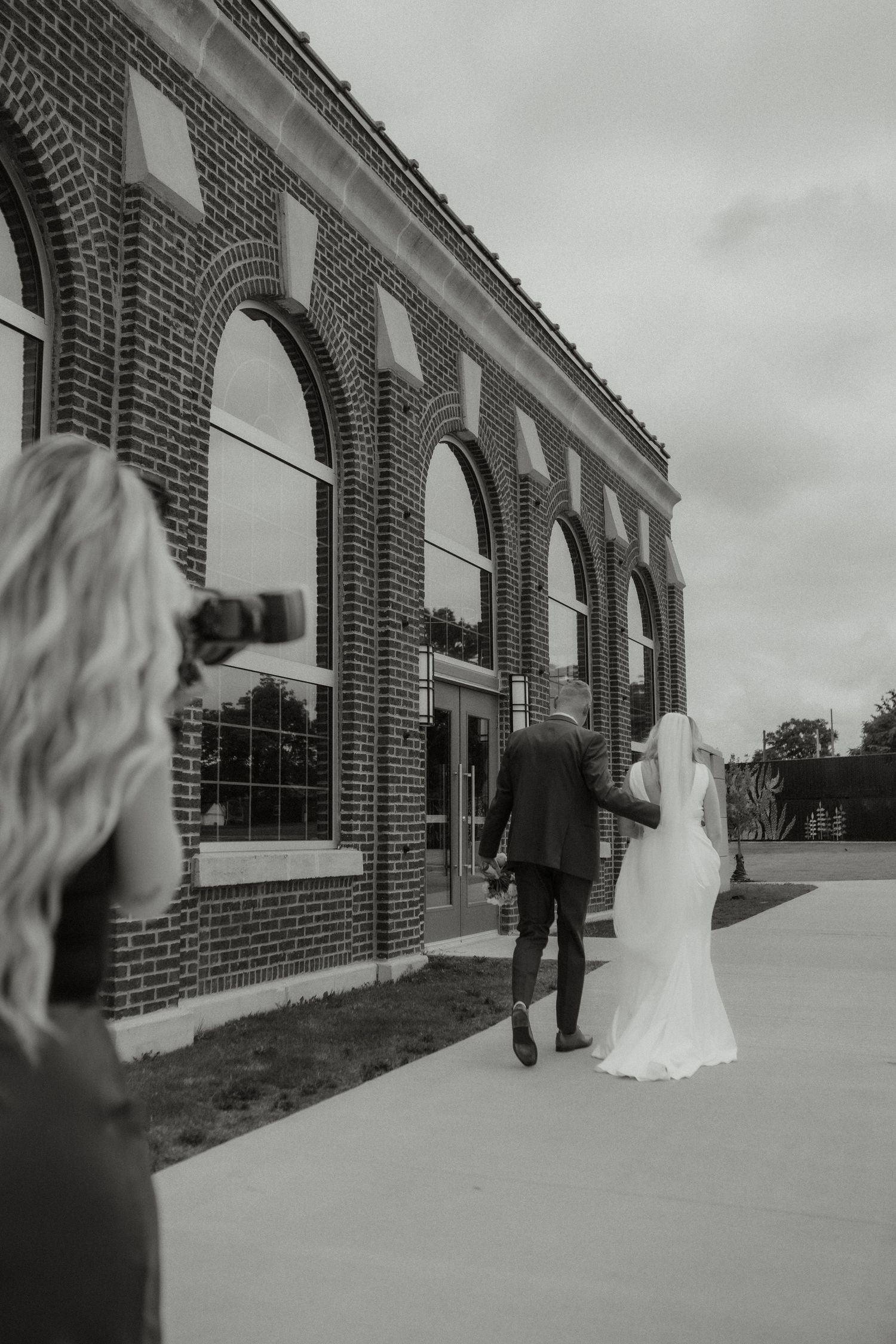 Black and white photo of photographer capturing bride and groom near brick building.