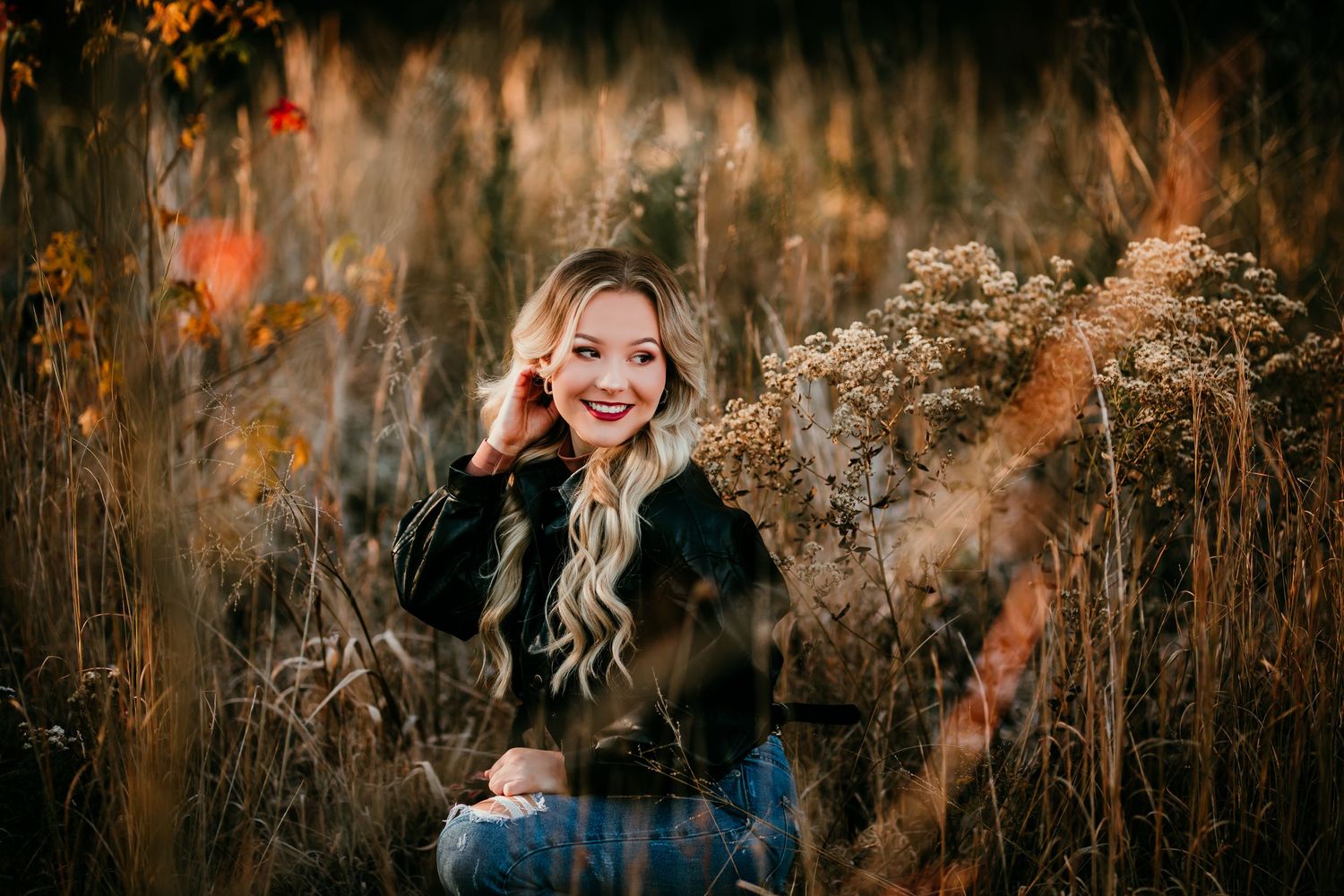 Smiling blonde woman sitting in autumn field with golden wildflowers.