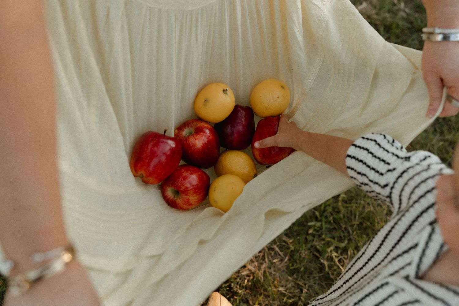 Woman in cream dress holding colorful fresh red apples and yellow lemons in her lap outdoors.