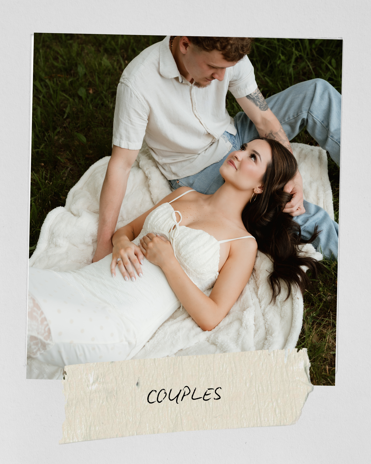 A romantic couples photo of a woman in a white dress resting on a man in a green field.