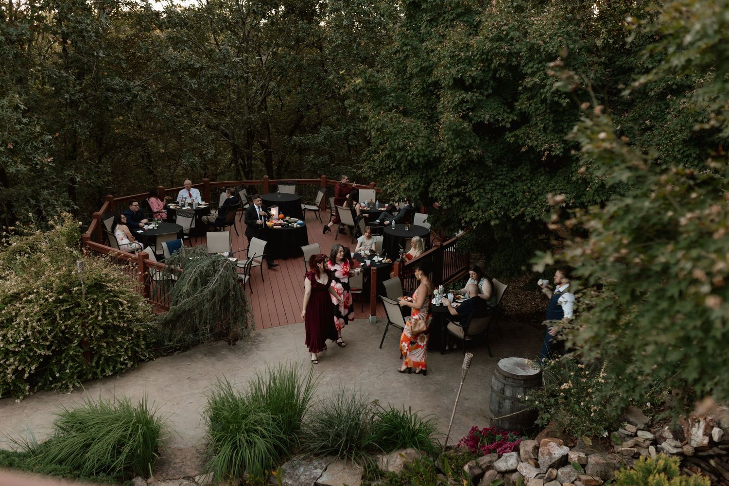Aerial view of wedding guests mingling at an outdoor garden reception surrounded by trees.