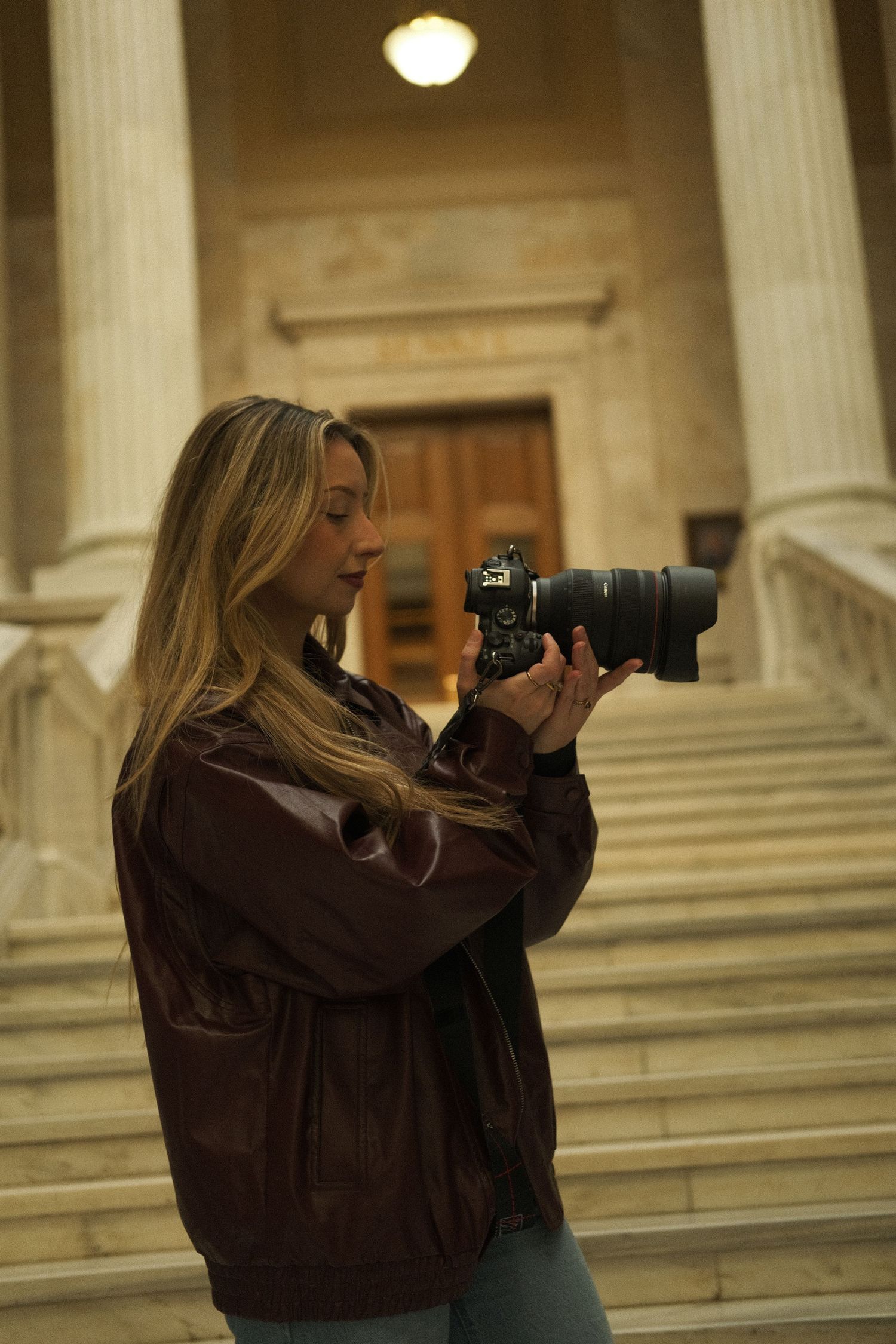 Young blonde woman reviewing photos on DSLR camera on steps of classical building.
