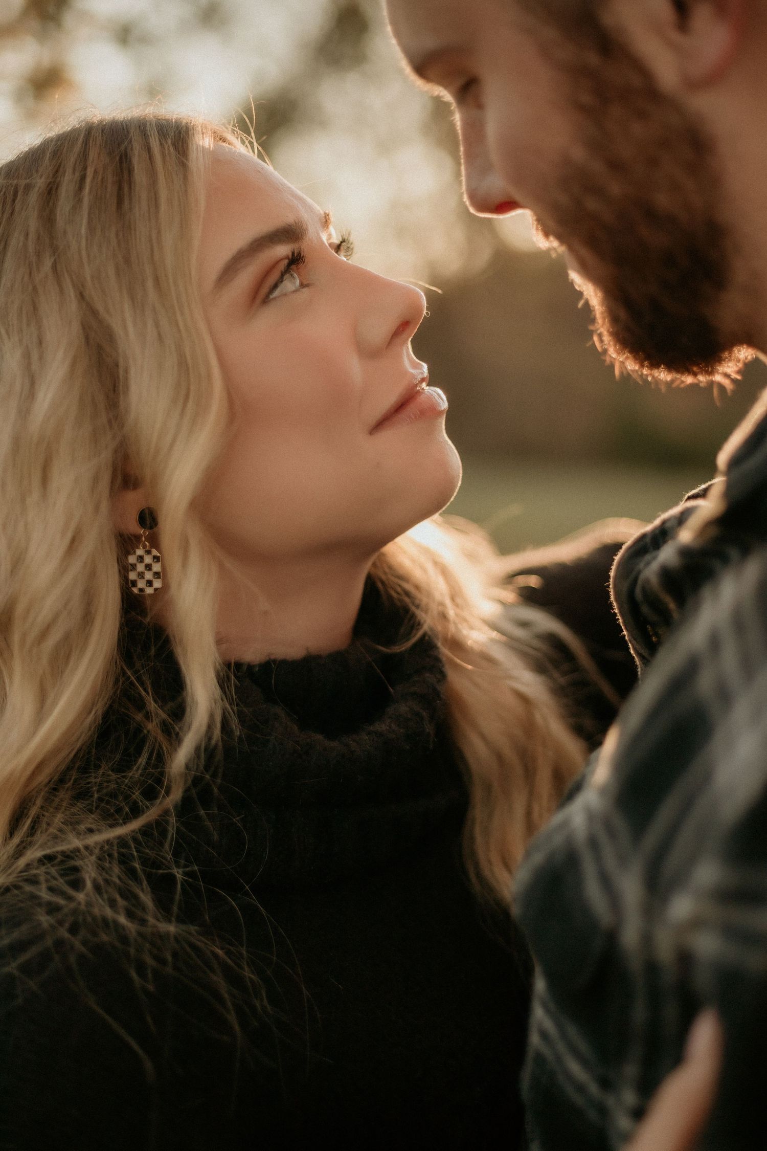 Couple shares an intimate almost-kiss moment outdoors, bathed in warm sunset backlight during engagement shoot.