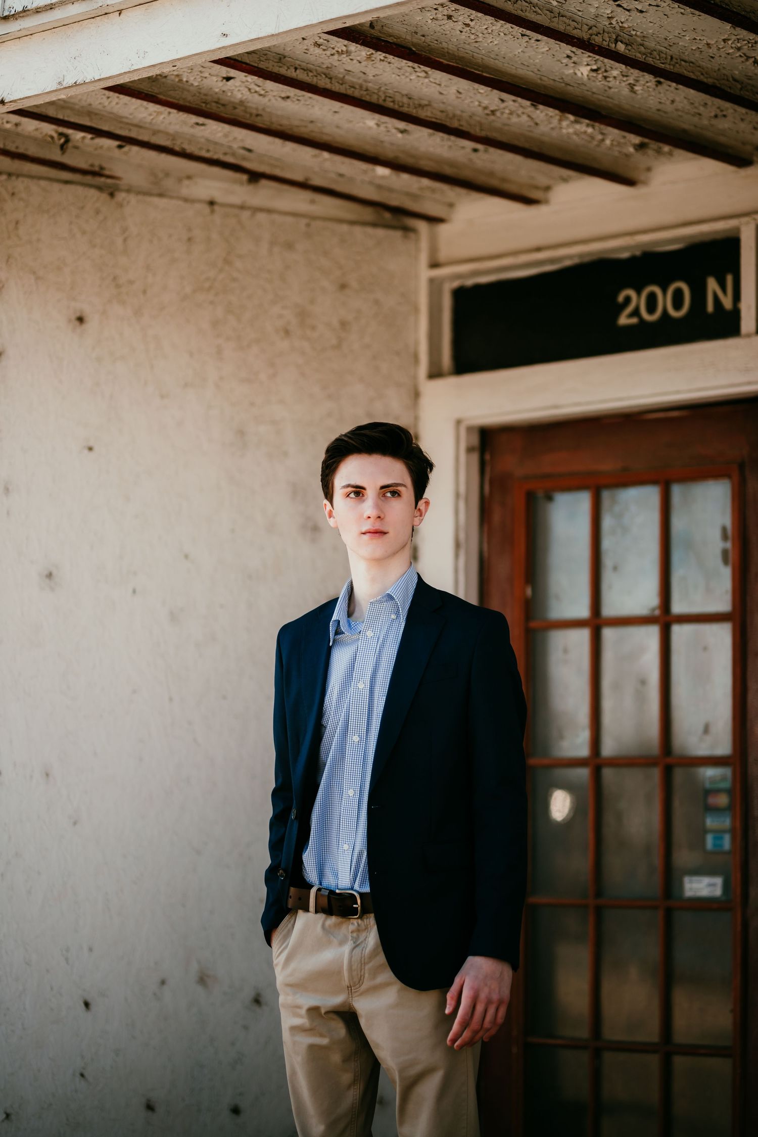 Young man in navy blazer stands confidently outside vintage building entrance marked 200 N.