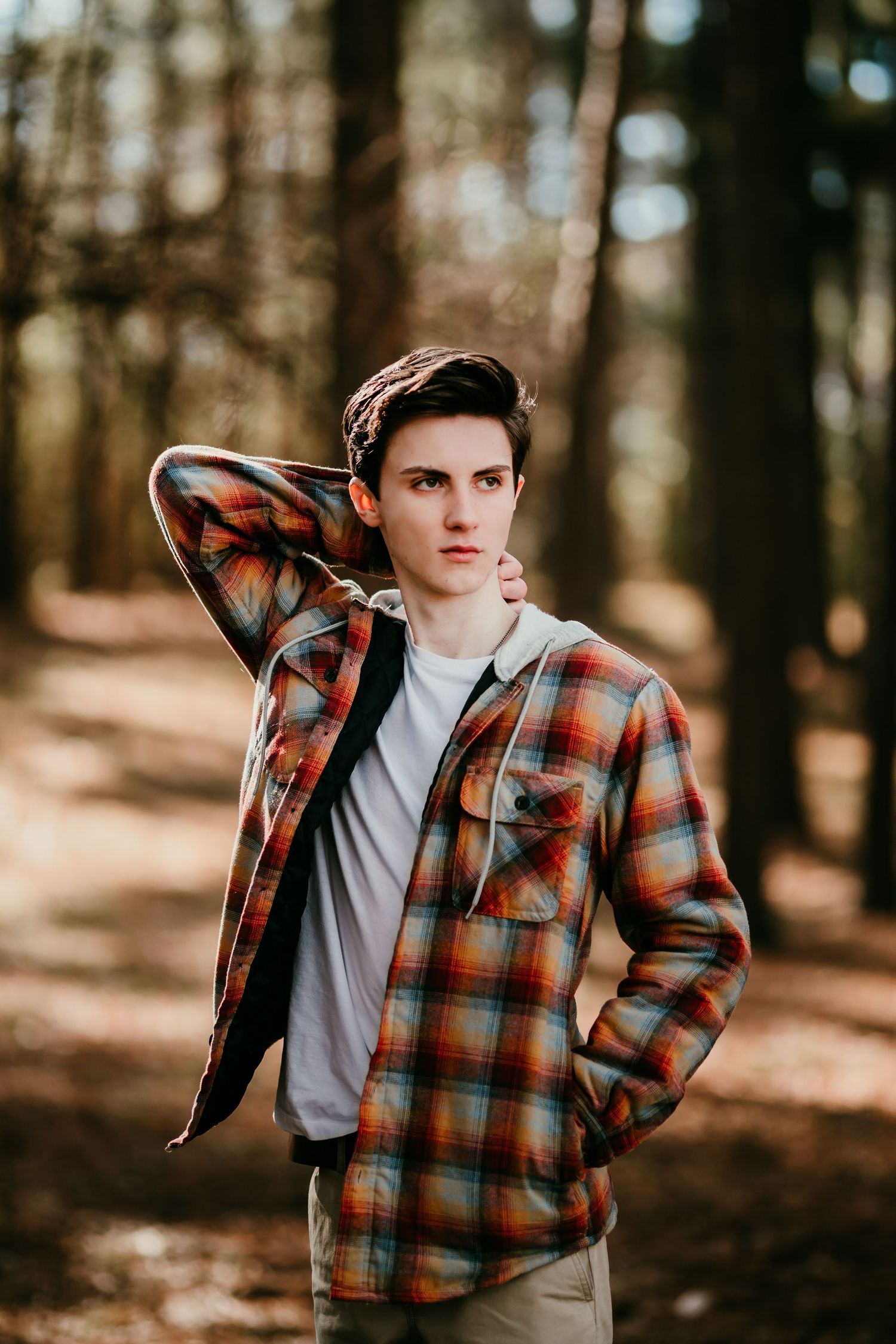 Teen boy in plaid flannel shirt posing in autumn forest with bokeh background.