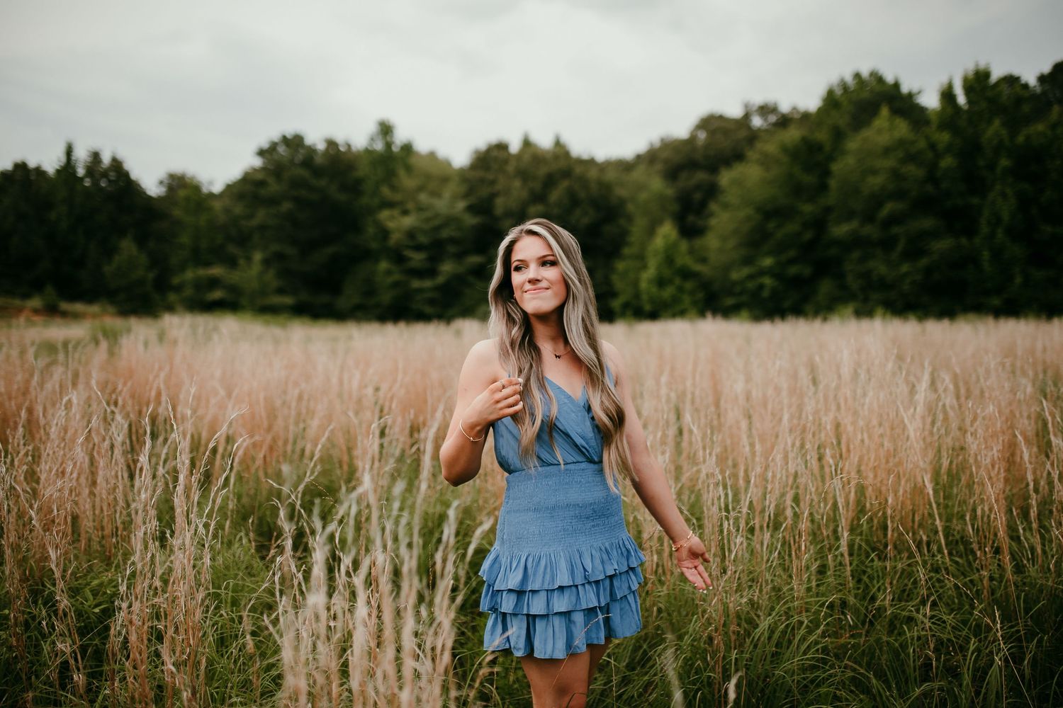 Blonde woman in blue ruffled mini dress stands gracefully in a tall golden grass field outdoors.
