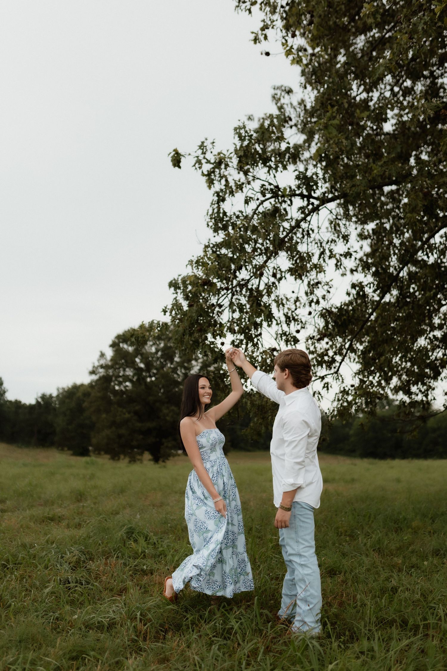 A couple dances together in a green field, the man spinning the woman in a light blue floral maxi dress.