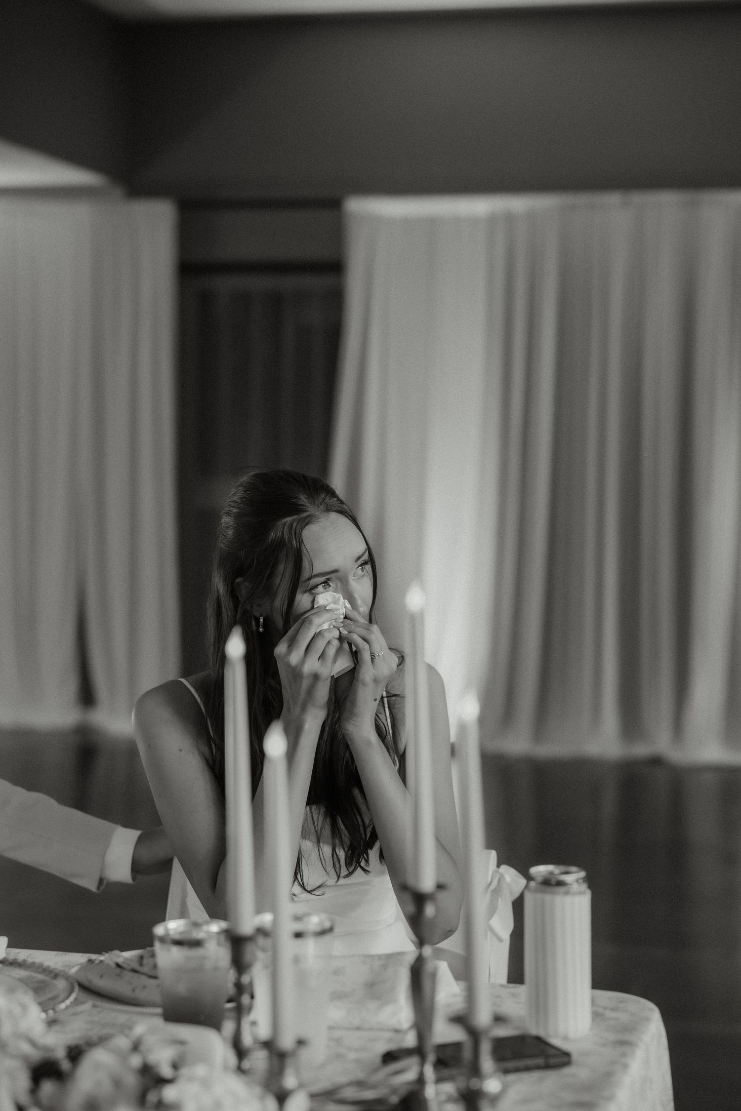 Bride crying tears of joy at candlelit wedding reception table in elegant black and white photo.
