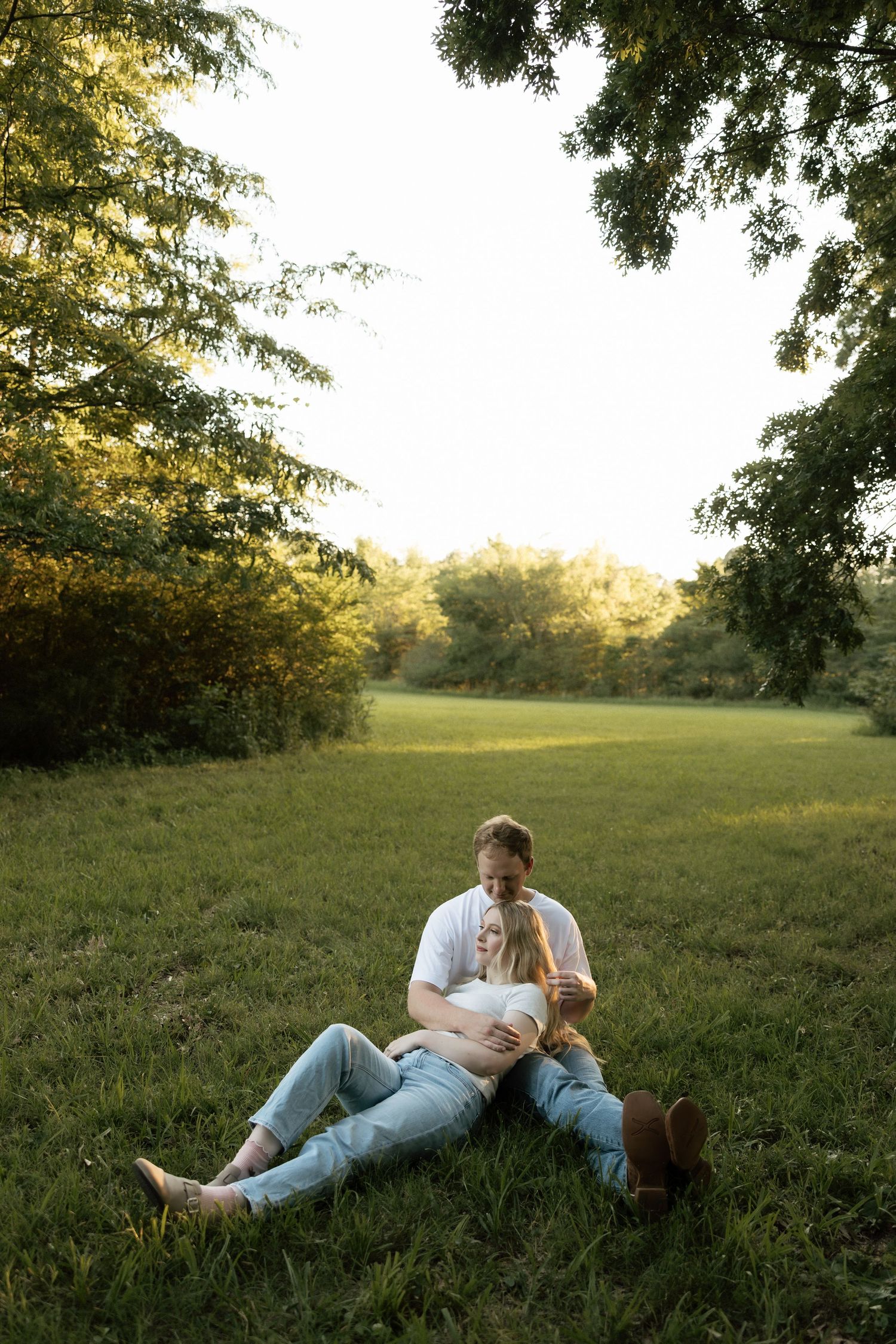 A couple relaxing on a green grassy field at sunset, with the woman leaning back against the man.