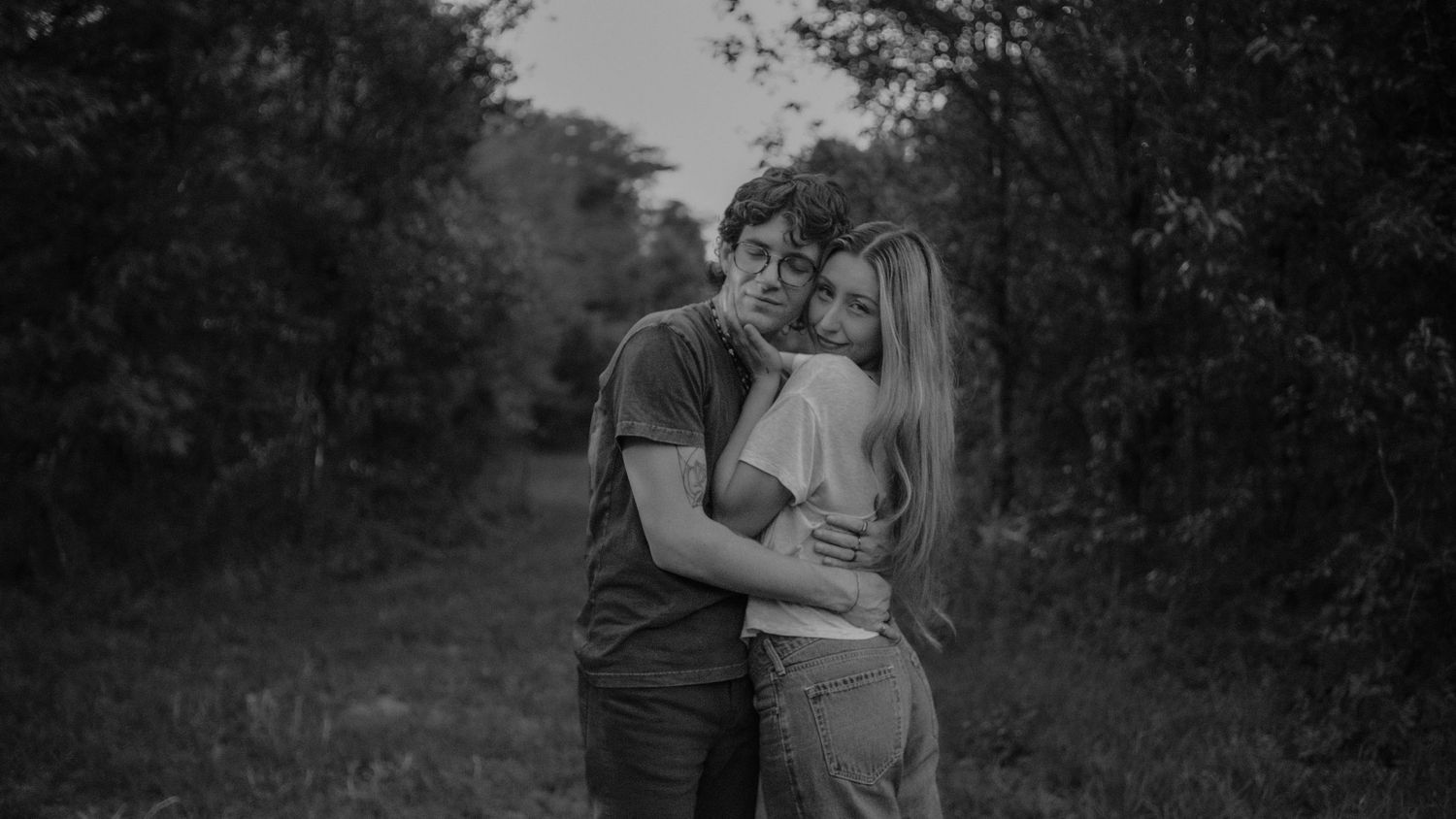 Romantic black and white couple embracing in a lush green field at dusk.