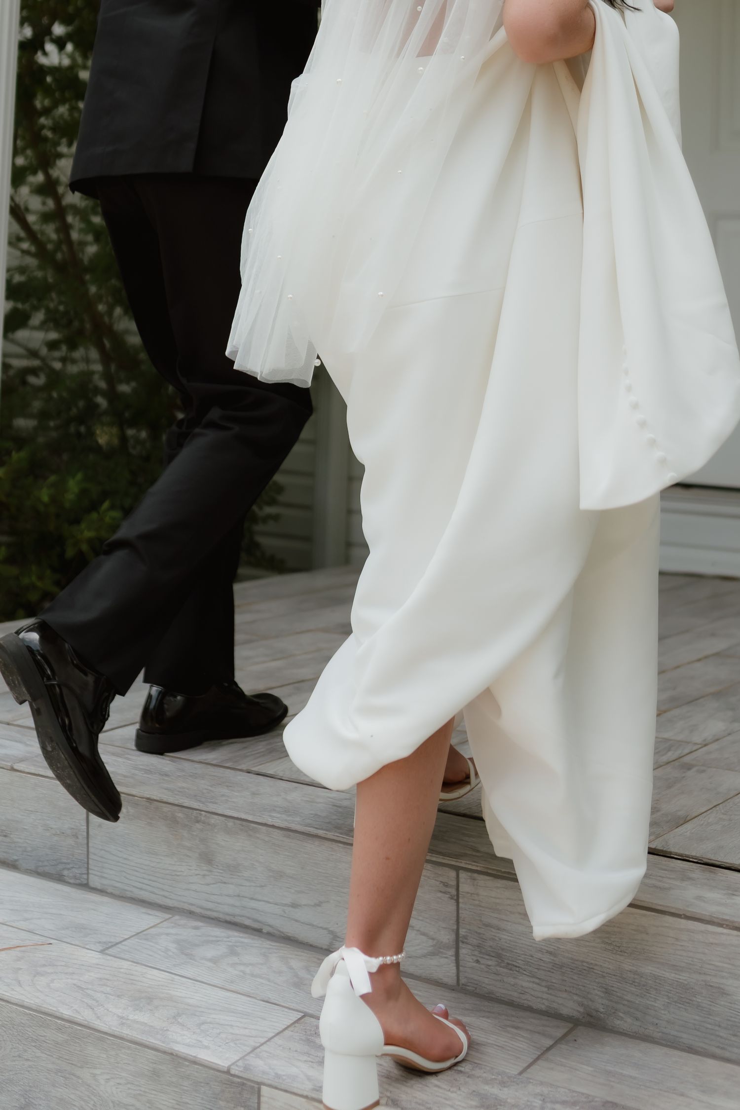Close-up of bride in white heels and groom in black dress shoes ascending marble steps.