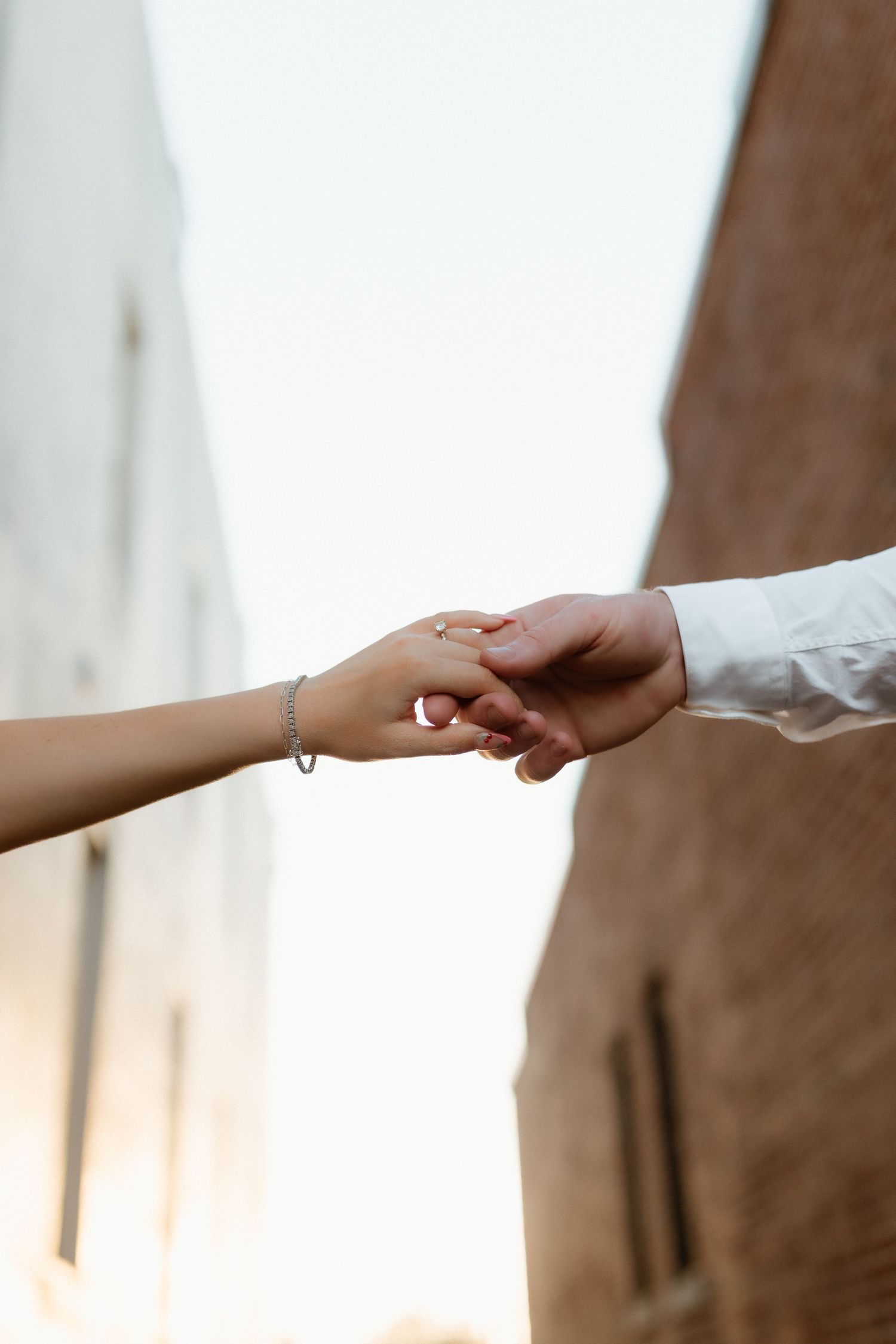 Close-up of a couple holding hands, woman wearing a bracelet and engagement ring outdoors.