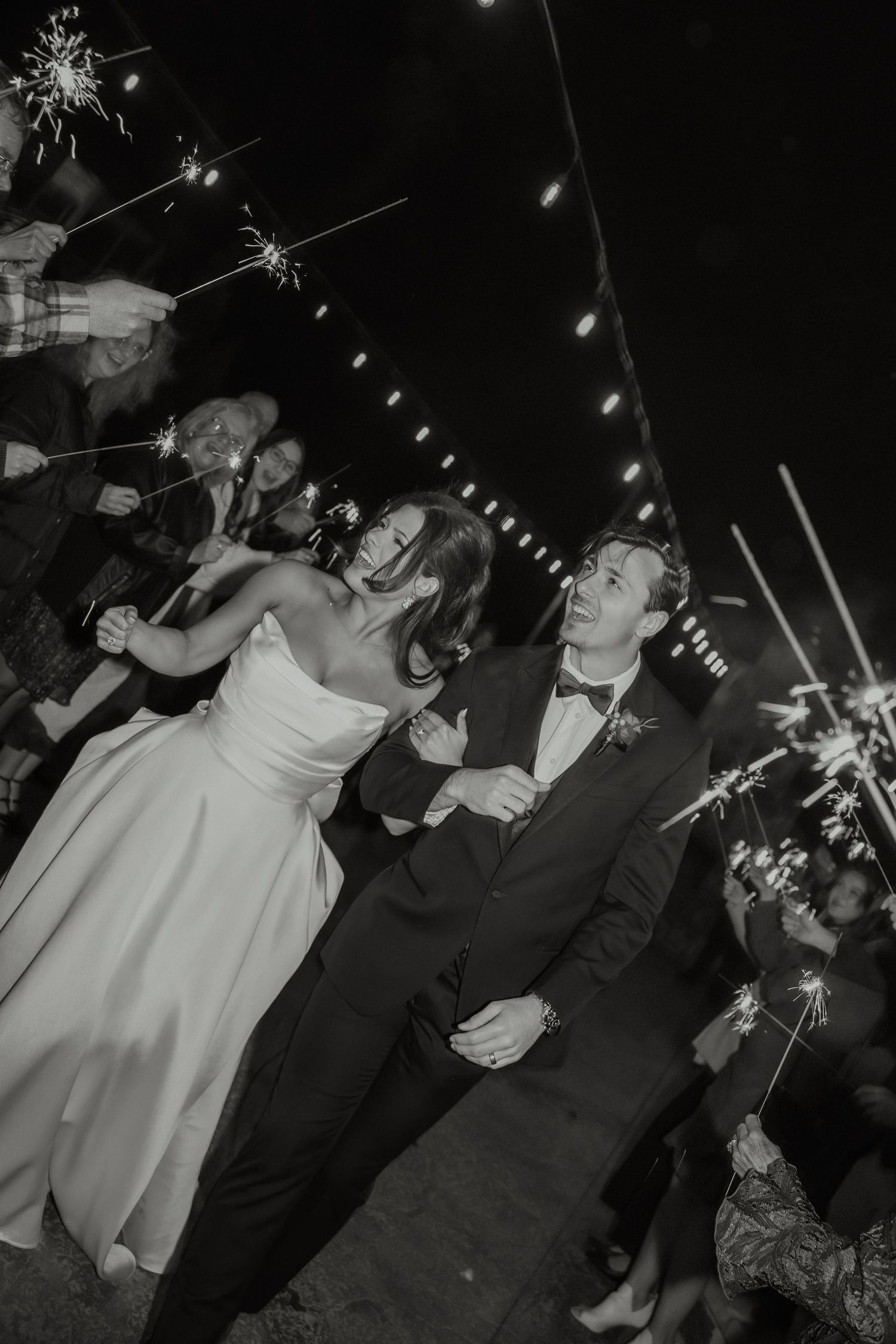 Black and white wedding photo of bride and groom walking through sparkler send-off at night reception.