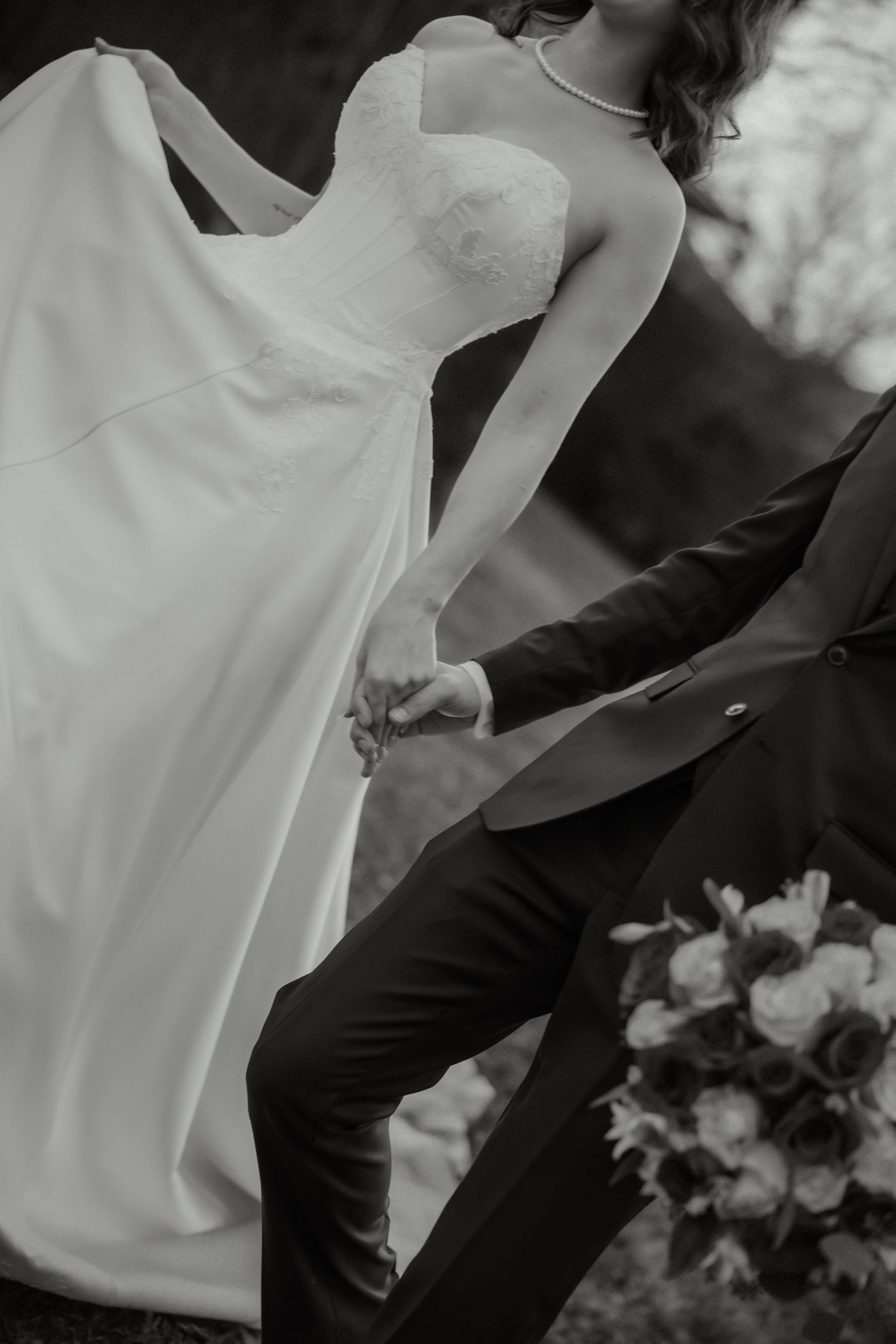 Black and white close-up of bride in strapless gown and groom holding hands with bouquet nearby.