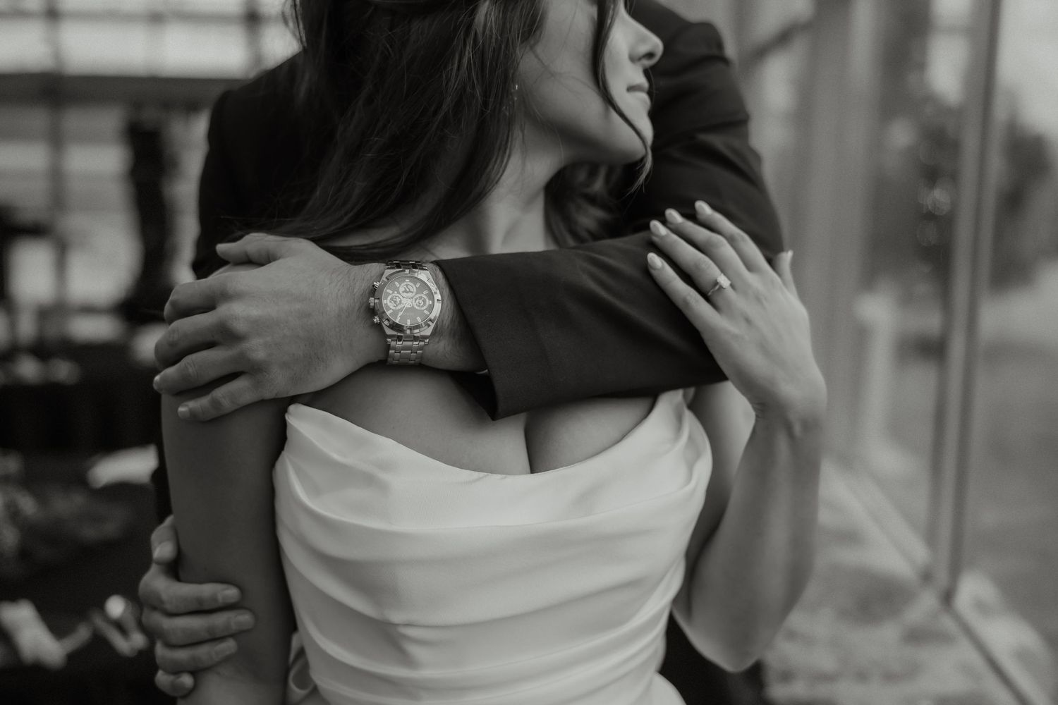 Intimate black and white close-up of groom embracing bride in strapless gown, showing watch detail.