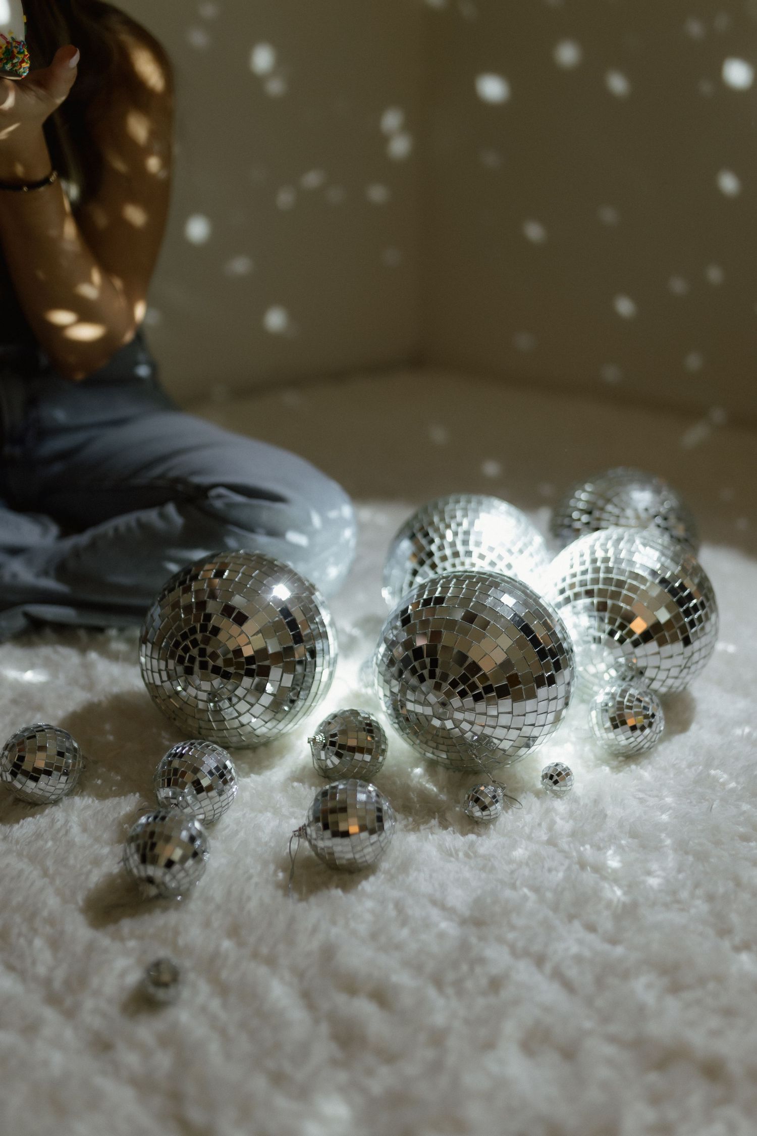 Shiny silver disco balls of various sizes arranged on a white fluffy surface.