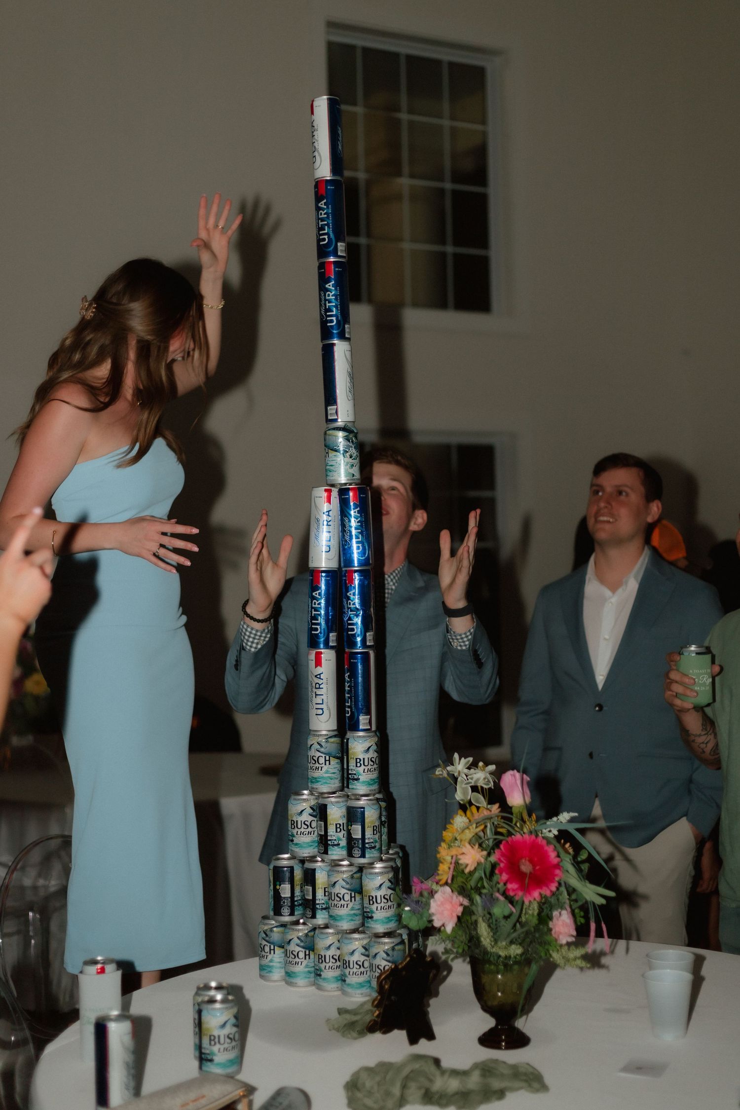 Wedding guests building a tower of beer cans on a reception table.