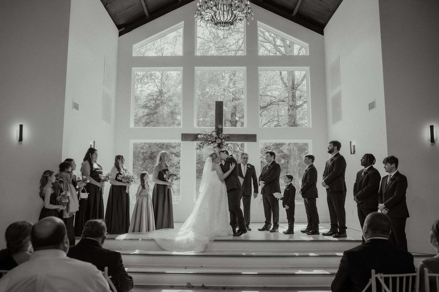 Bride and groom exchanging vows at altar in elegant chapel with large window.