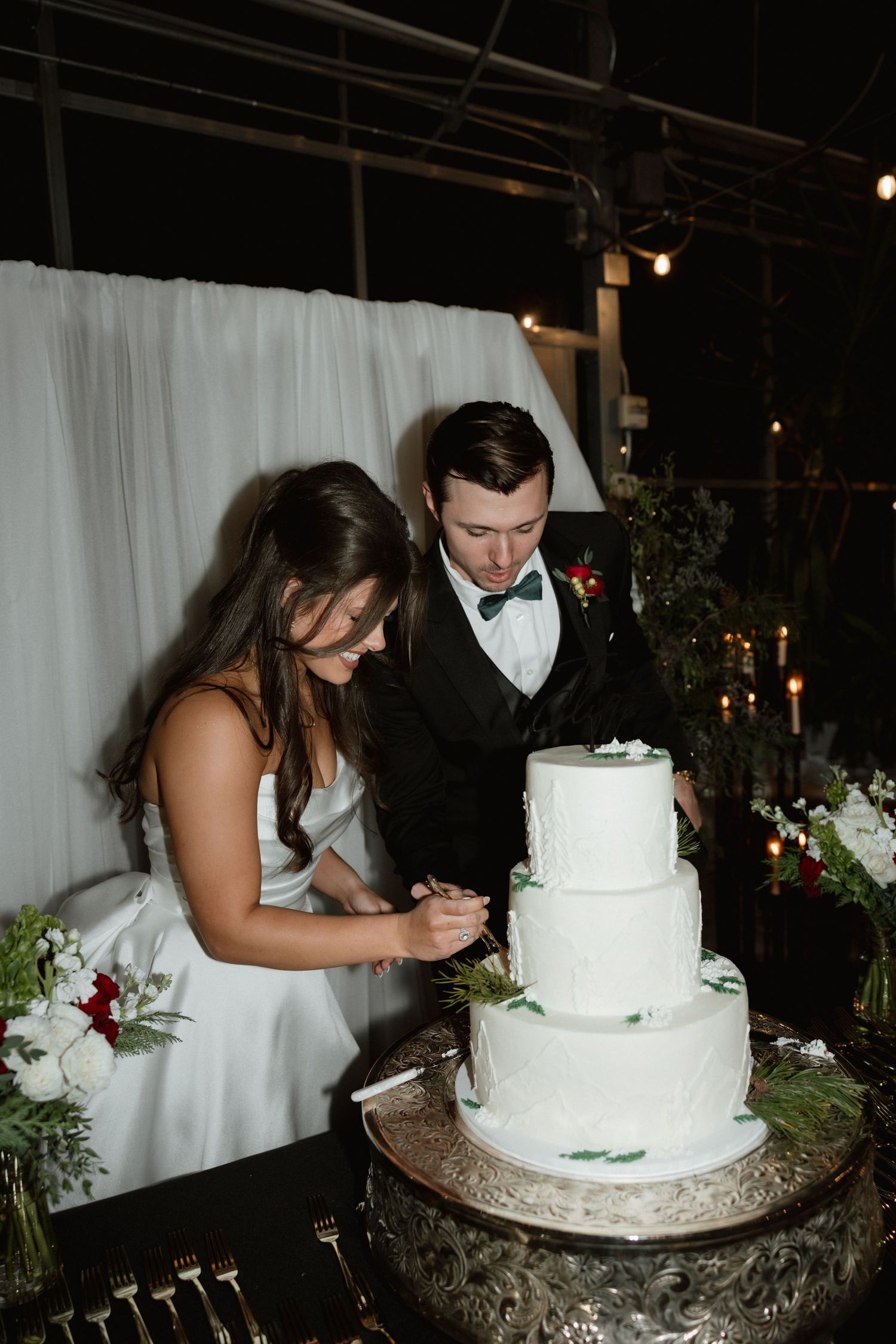 Bride and groom cutting white three-tier wedding cake at evening reception.