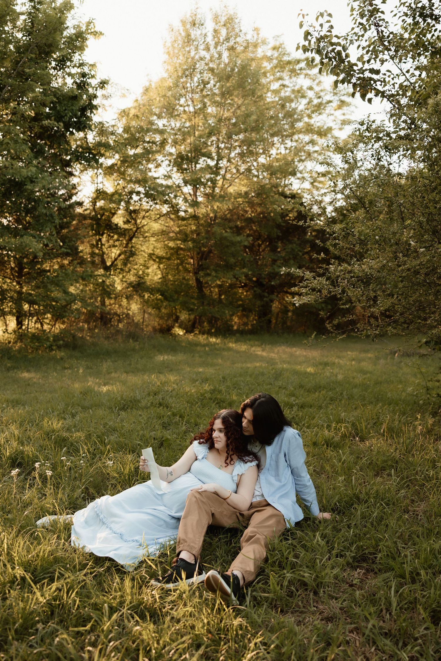 Couple sitting together in a sunlit grassy field, woman leaning on mans shoulder at sunset.