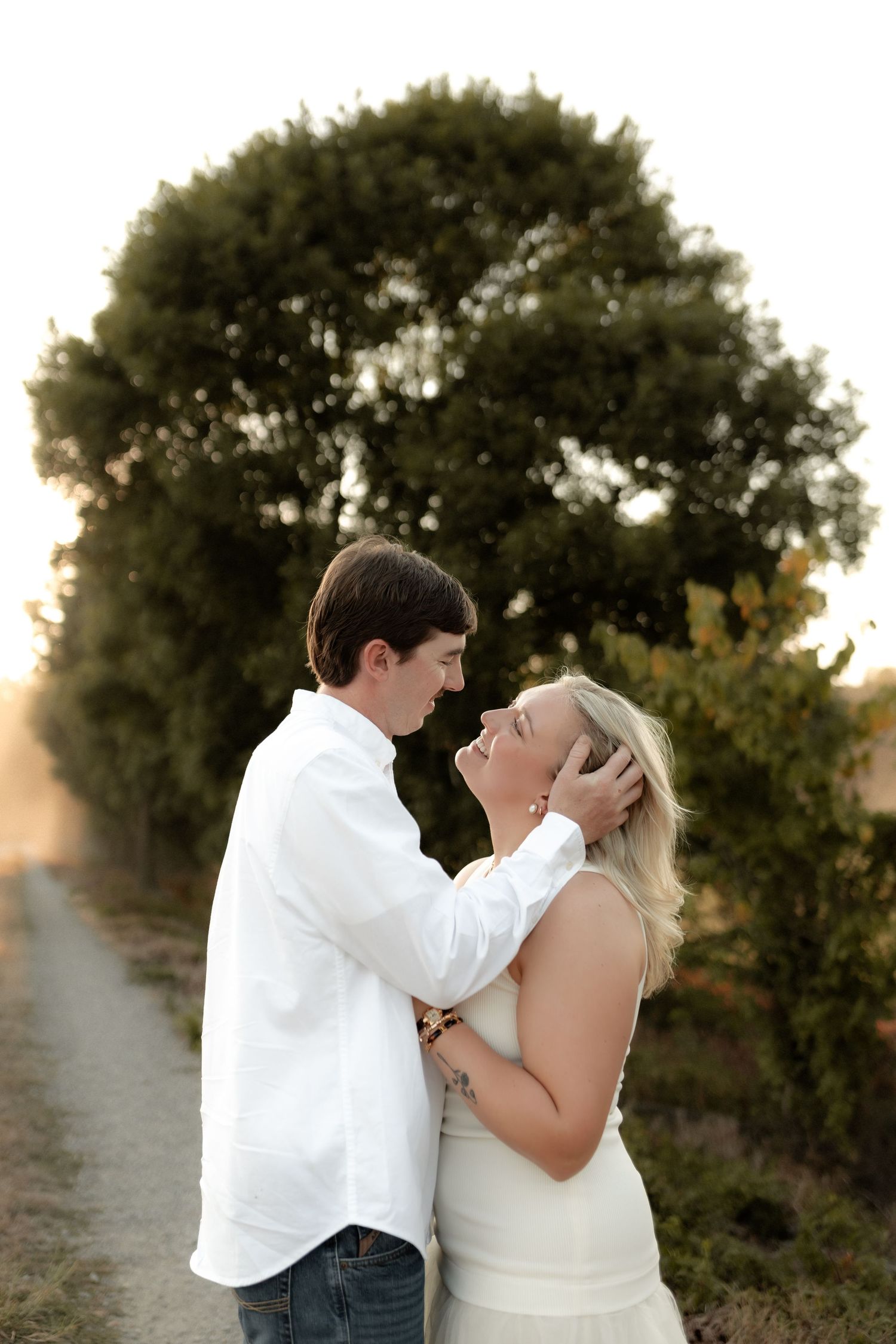 Groom tenderly holding brides face as they lean in for a kiss at sunset.