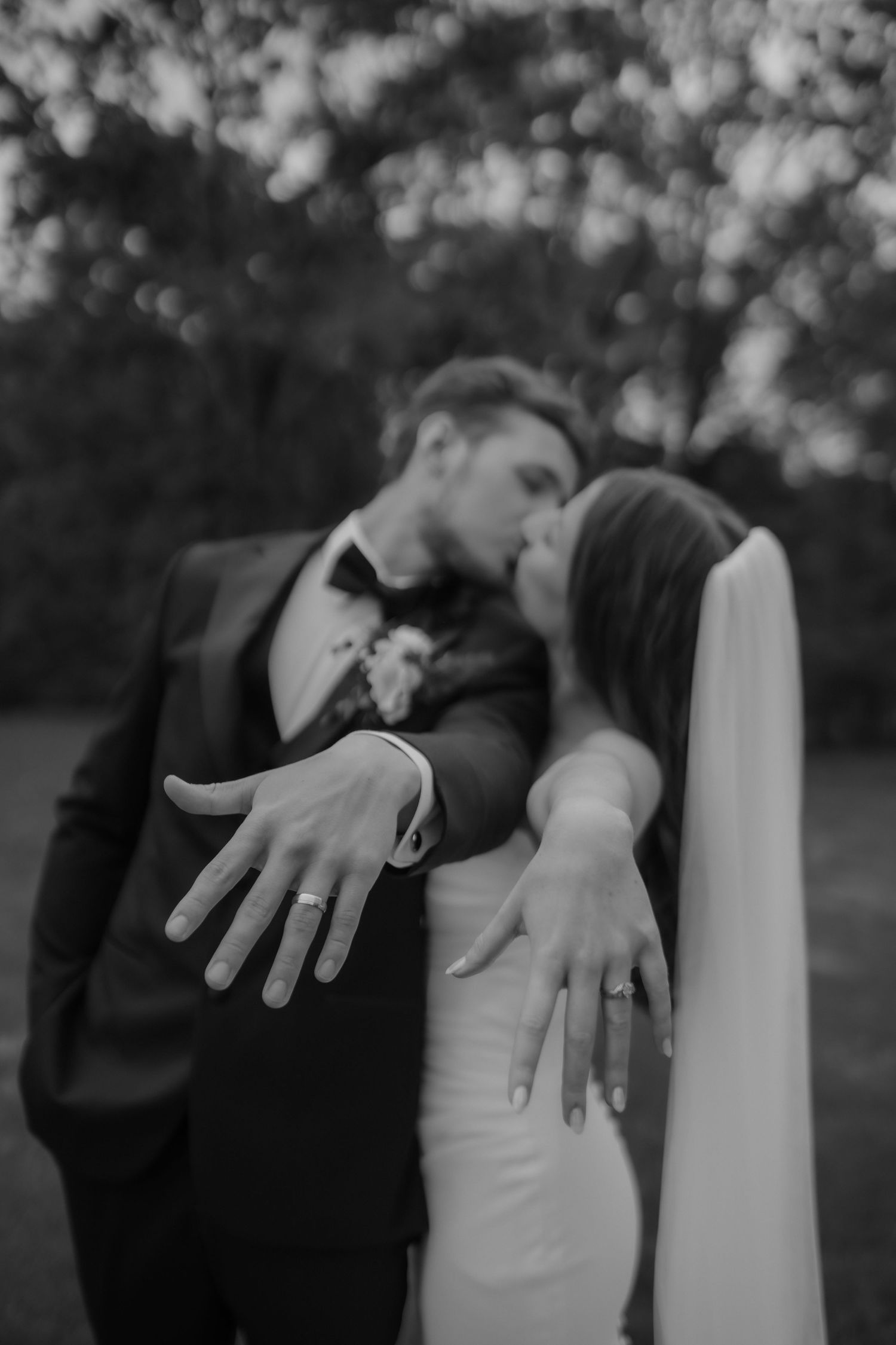 Newlyweds kissing while showing off wedding rings in black and white photo.