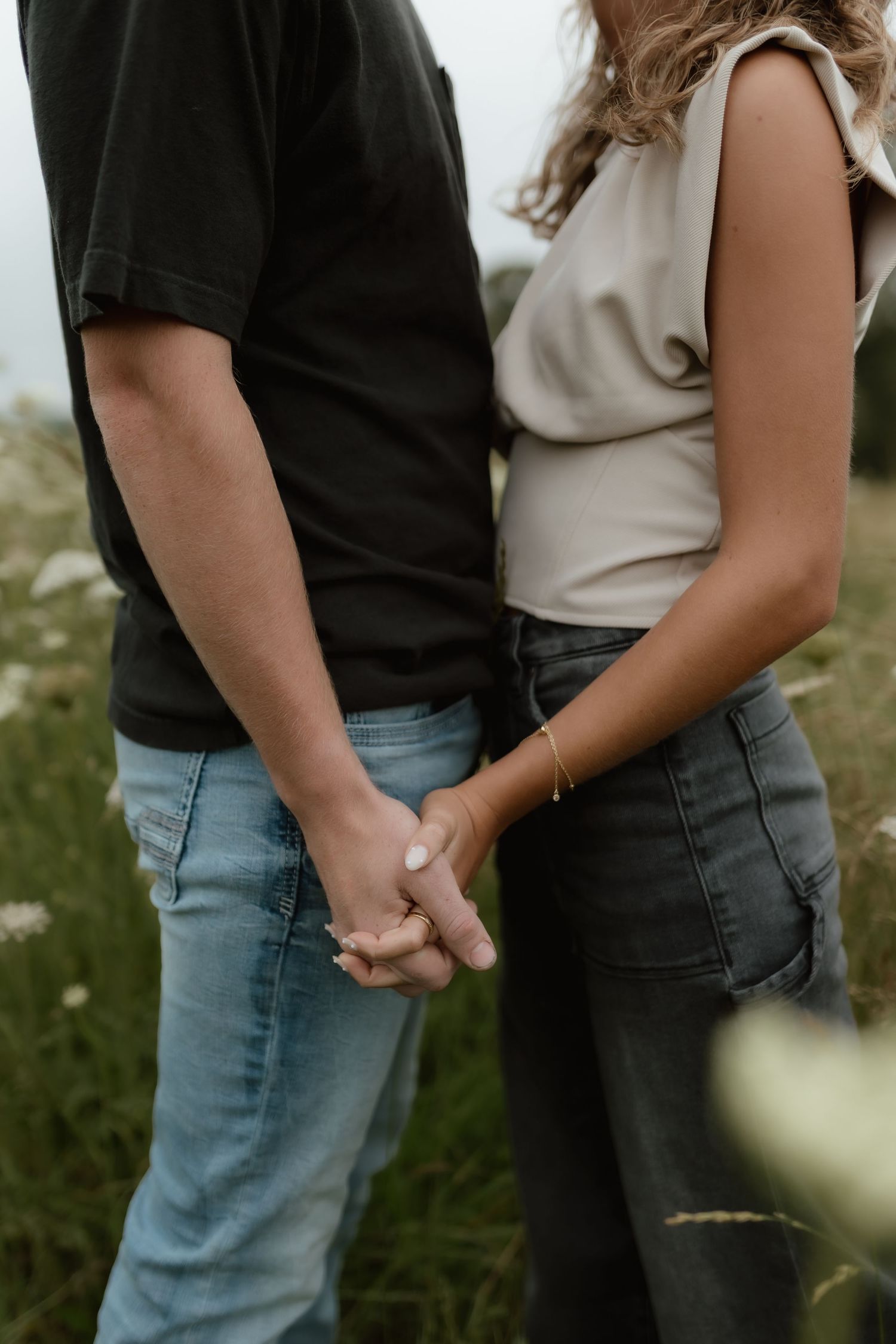 Couple holding hands in a wildflower field, man in black tee and blue jeans, woman in beige top and gray jeans.