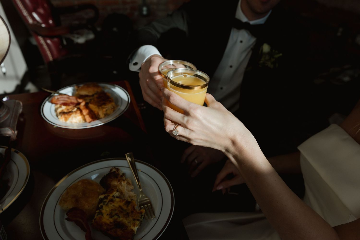 Bride and groom clink glasses over dinner plates at their wedding reception.